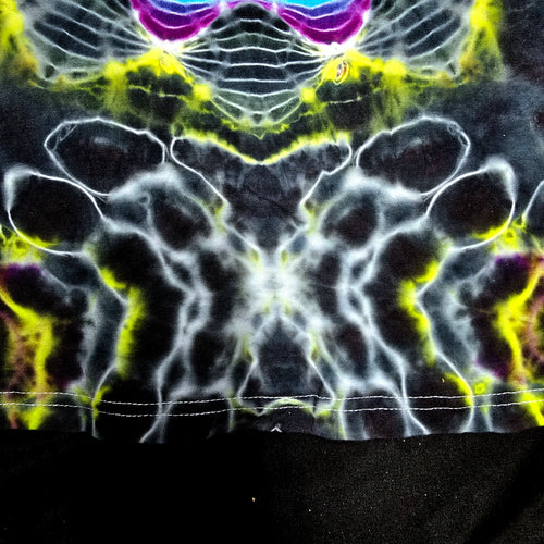 Close-up of a black fabric with a highly reflective, symmetrical chrome or metallic foil pattern in white, bright yellow, and purple.