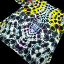 A close-up of a tie-dye fabric or material sample with a spiral pattern in black, white, blue, purple, and bright yellow, shown against a black background.