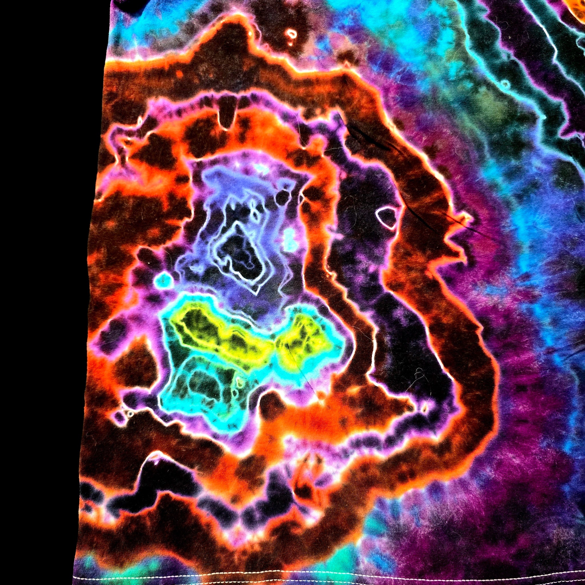 A close-up of a tie-dye fabric featuring a vibrant concentric agate-geode pattern with neon orange, purple, blue, green, and yellow hues.