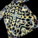 A close-up of a black fabric or material sample with a repeating honeycomb-like pattern outlined in glowing yellow, blue, and white, shown against a black background.