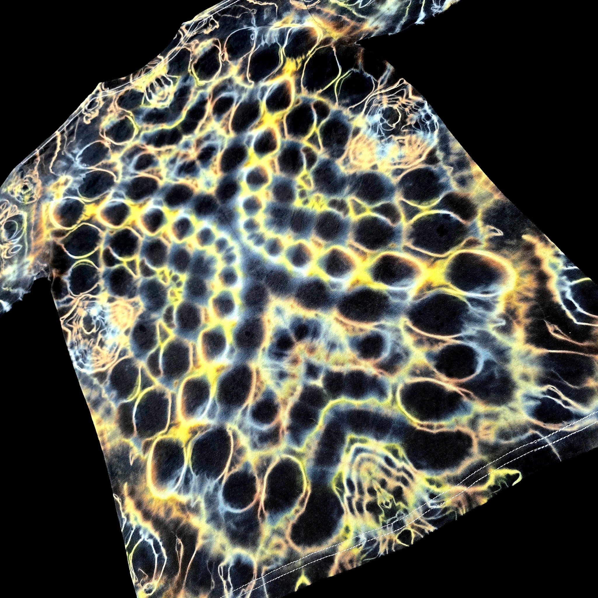 A close-up of a black fabric or material sample with a repeating honeycomb-like pattern outlined in glowing yellow, blue, and white, shown against a black background.