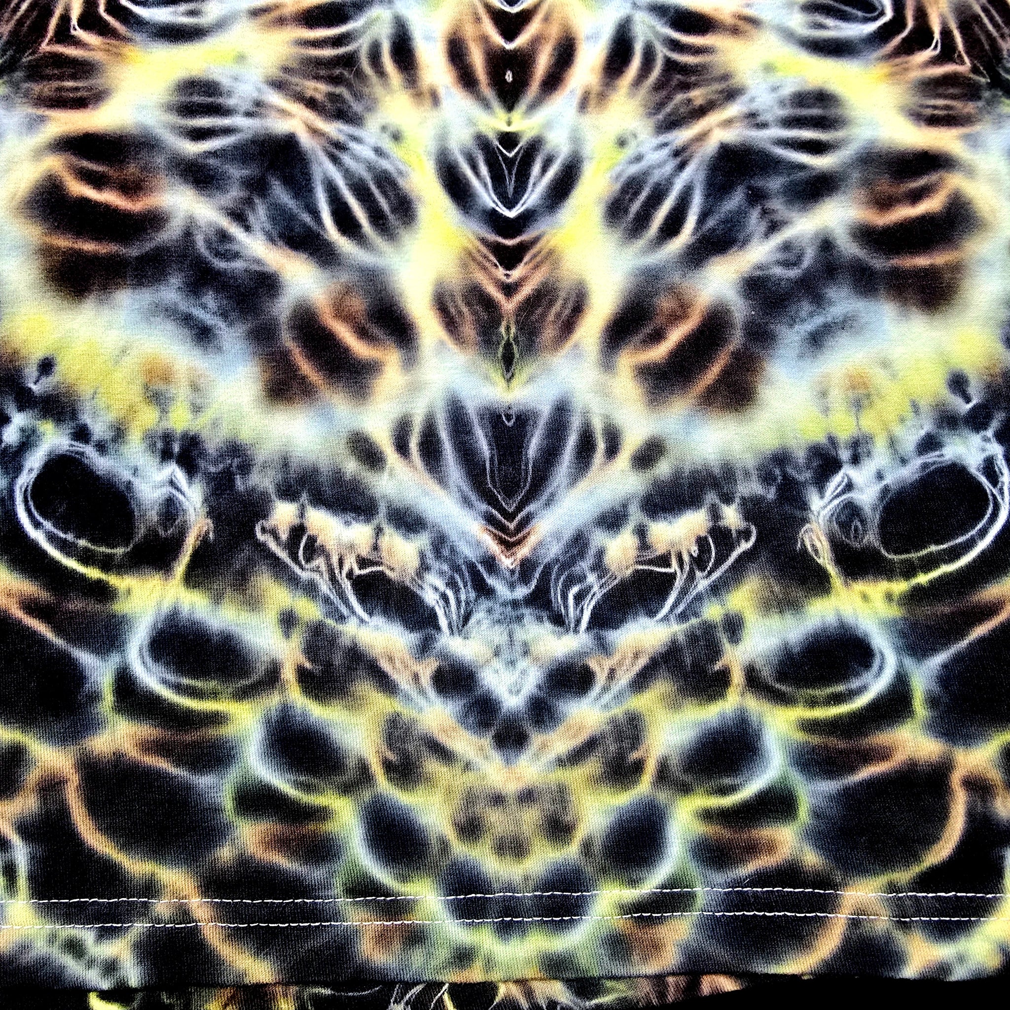 A close-up of a fabric surface with a symmetrical, psychedelic tie-dye pattern in black, yellow, white, and orange-brown.