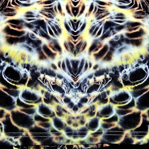 A close-up of a fabric surface with a symmetrical, psychedelic tie-dye pattern in black, yellow, white, and orange-brown.