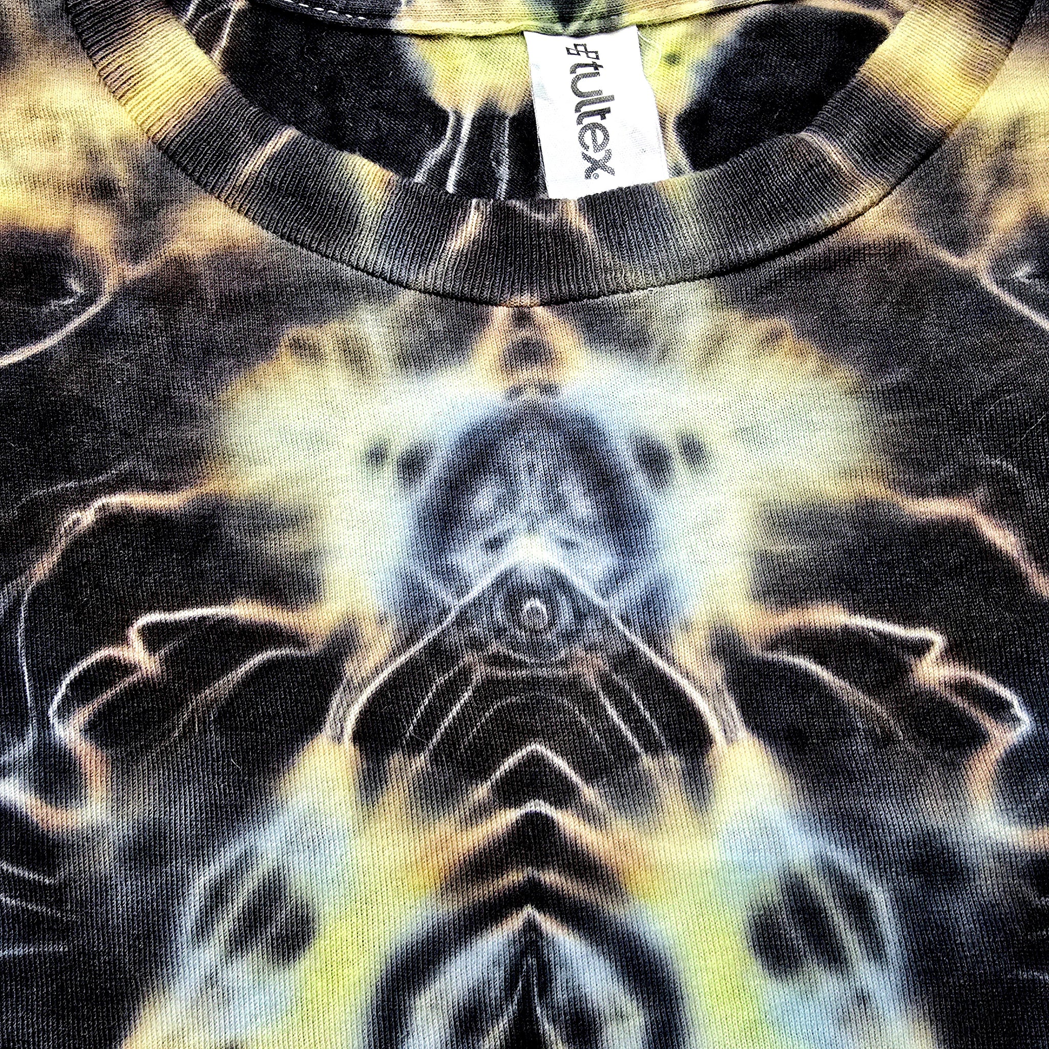 Close-up of a tie-dye t-shirt featuring a symmetrical, kaleidoscopic pattern in black, yellow, and white. The brand tag 'fullex' is visible inside the collar.