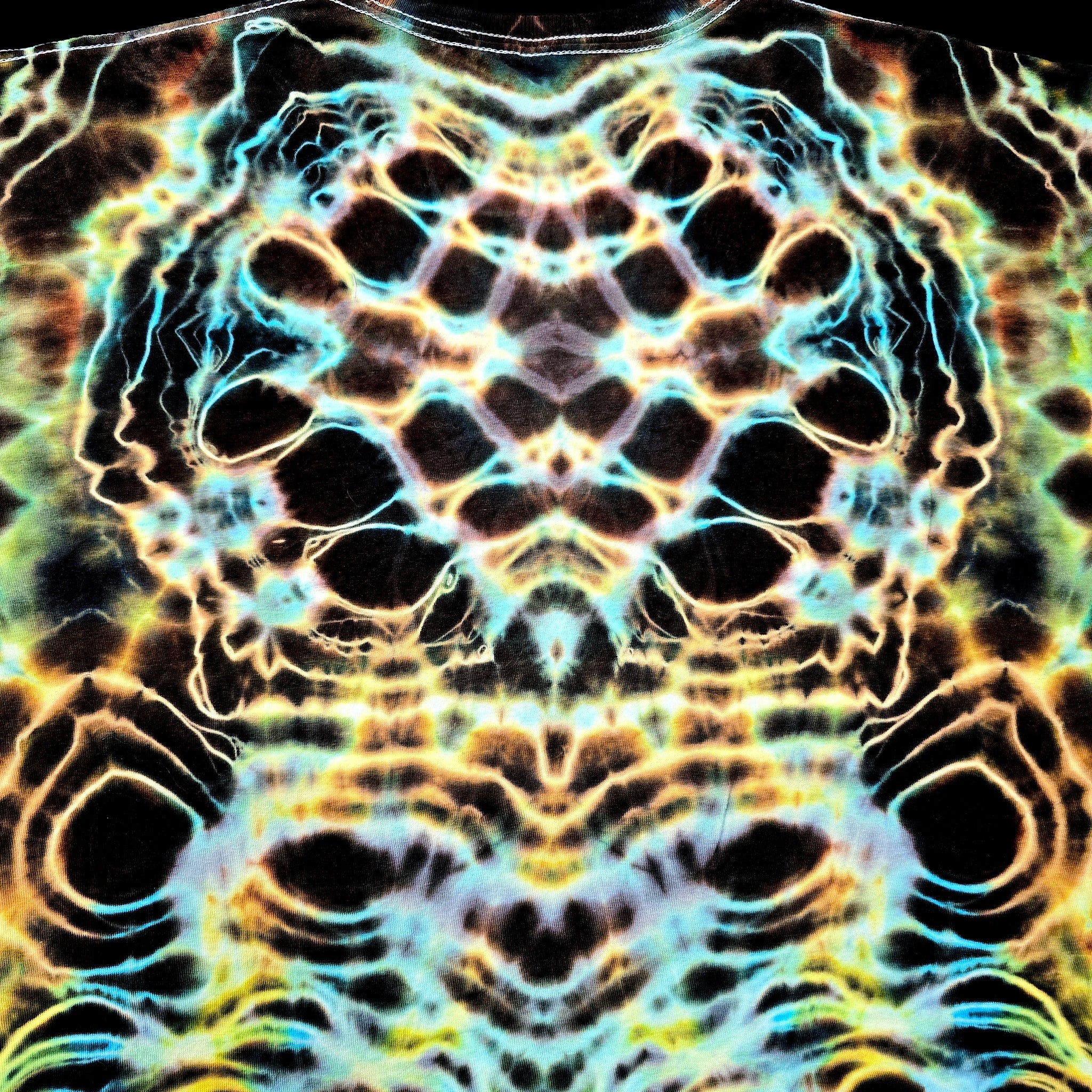 A close-up of a highly patterned fabric featuring a symmetrical, kaleidoscopic design with black, neon yellow, cyan, and orange tones.