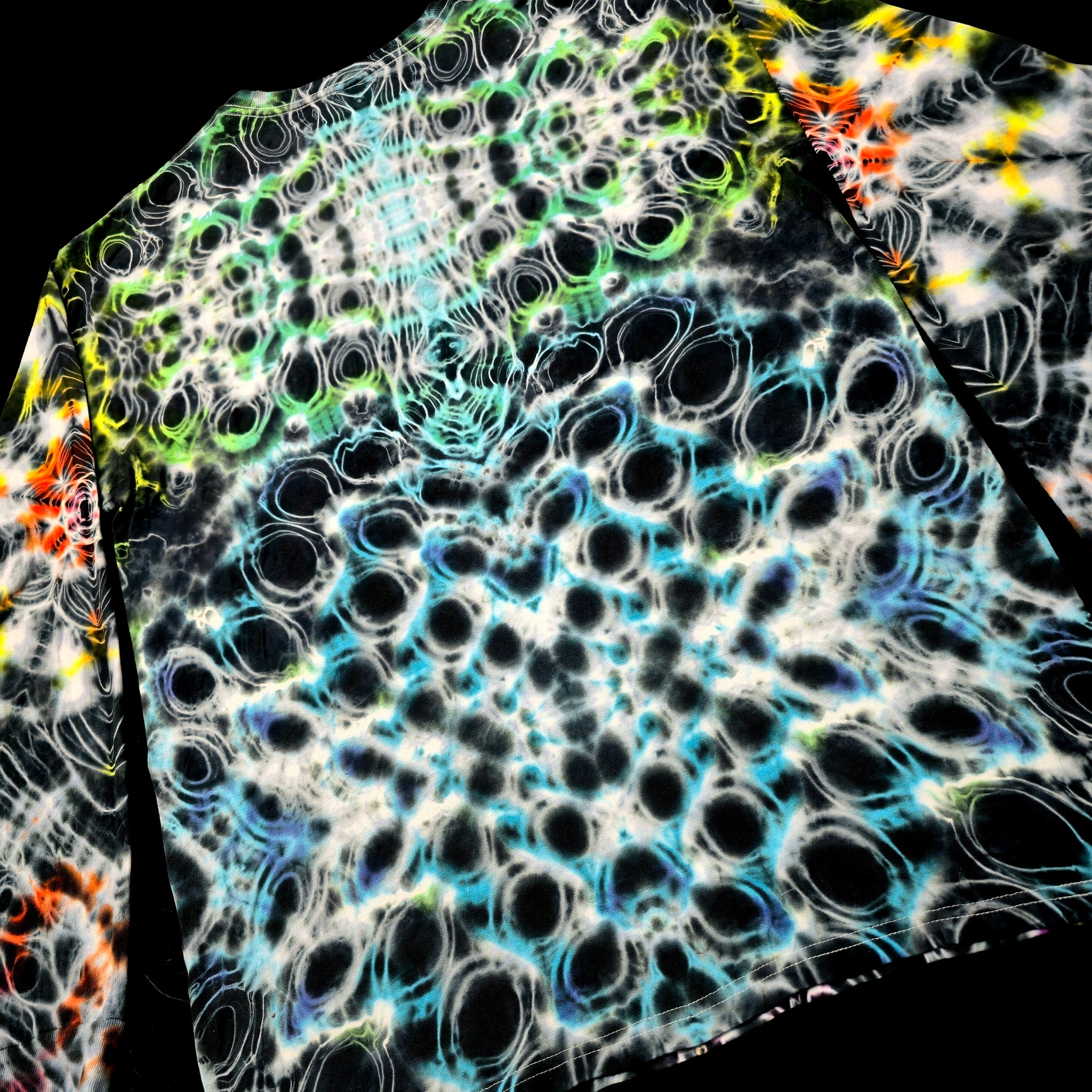 A close-up of a garment featuring a complex, high-contrast abstract pattern with black, white, blue, green, and orange circular and bubble-like motifs on a dark background.
