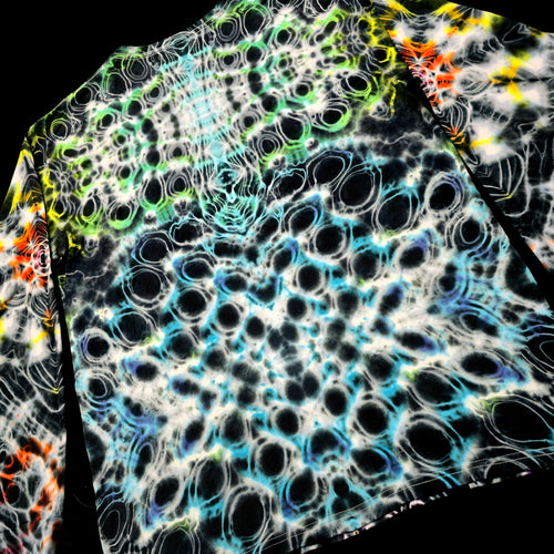 A close-up of a garment featuring a complex, high-contrast abstract pattern with black, white, blue, green, and orange circular and bubble-like motifs on a dark background.