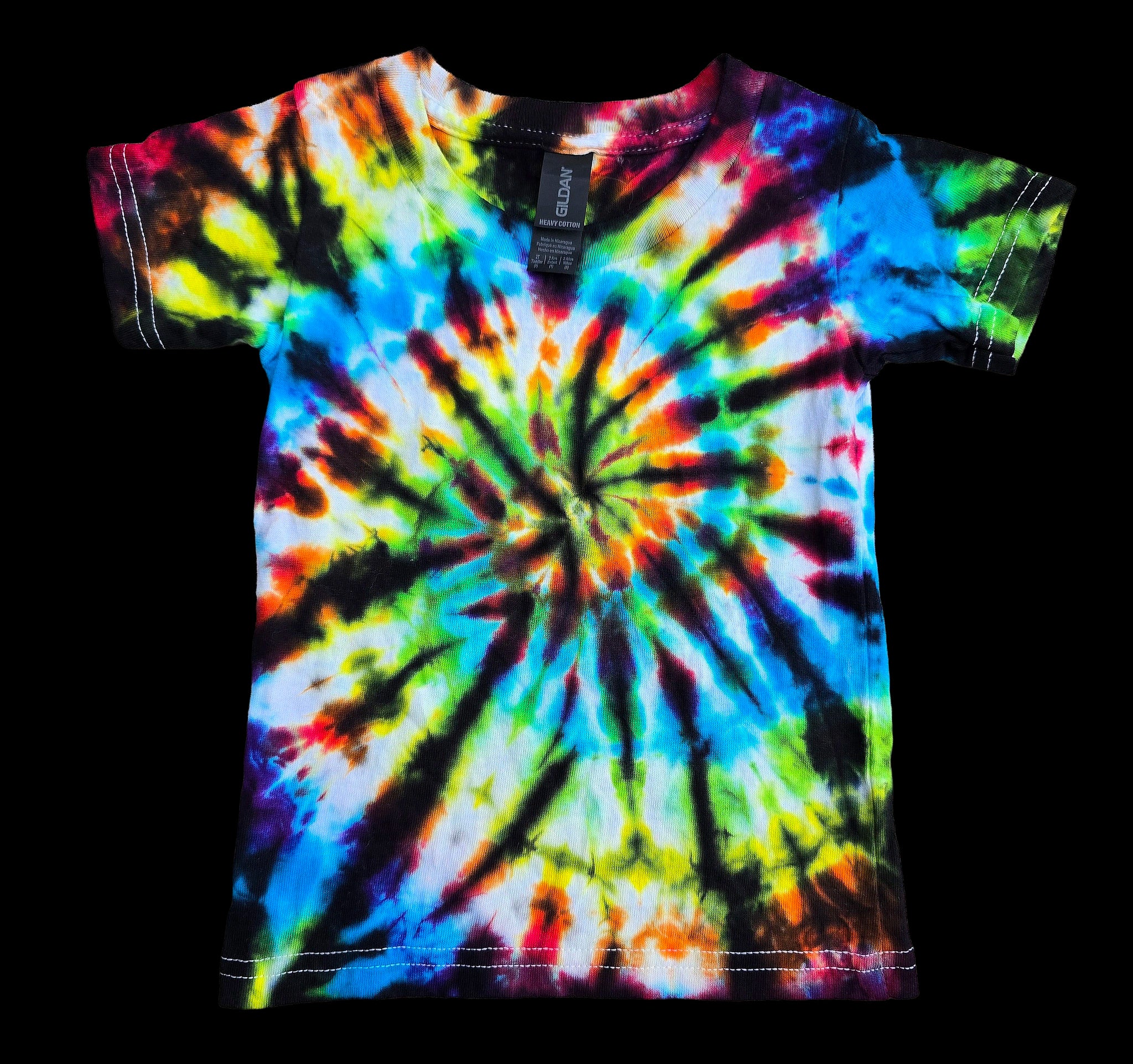 A short-sleeve tie-dye t-shirt with a vibrant spiral pattern in blue, green, yellow, orange, red, and black, laid flat against a solid black background. A brand tag for 'Society6' is visible at the collar.