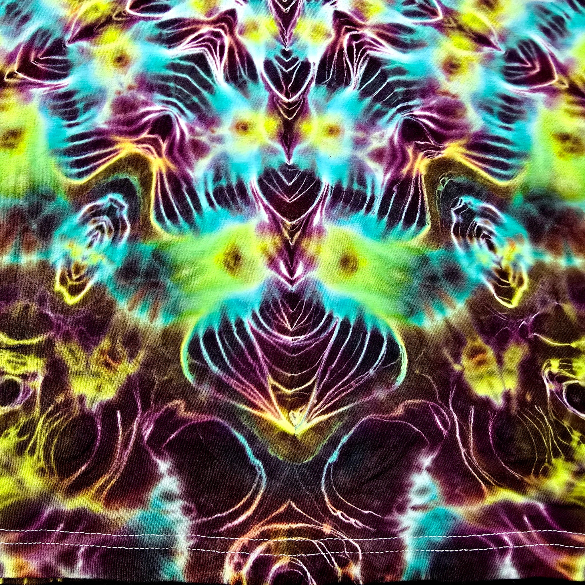 A close-up of a psychedelic tie-dye fabric with a symmetrical, kaleidoscopic pattern in neon purple, cyan, lime green, yellow, and black.