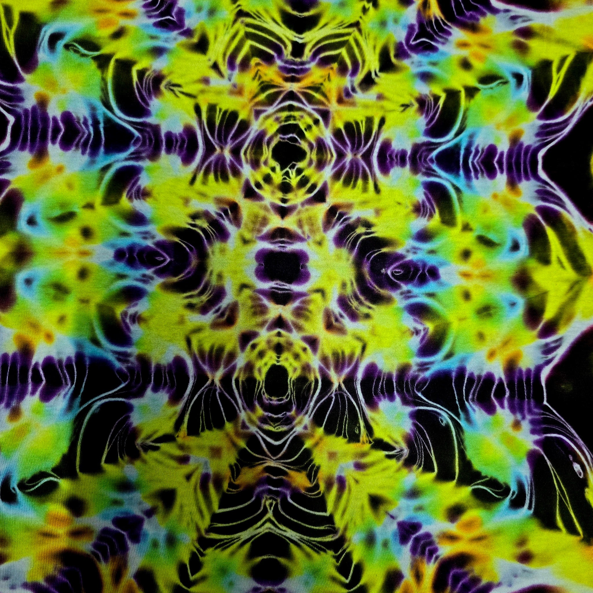 A close-up of a psychedelic tie-dye pattern with symmetrical, kaleidoscopic swirls of neon yellow, lime green, purple, blue, and black.