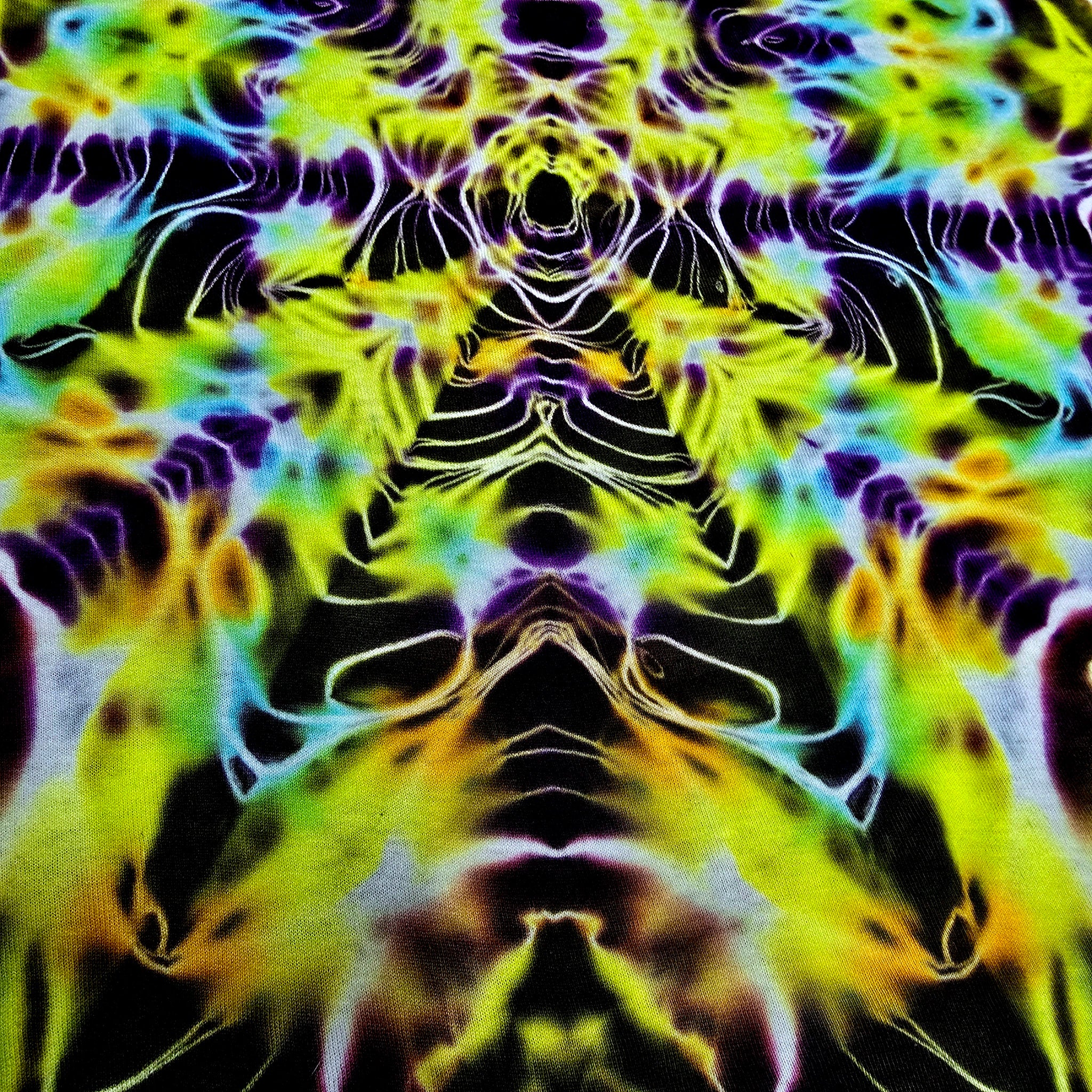 A close-up of a psychedelic tie-dye fabric with a symmetrical, kaleidoscopic pattern in neon yellow, green, purple, blue, and black.