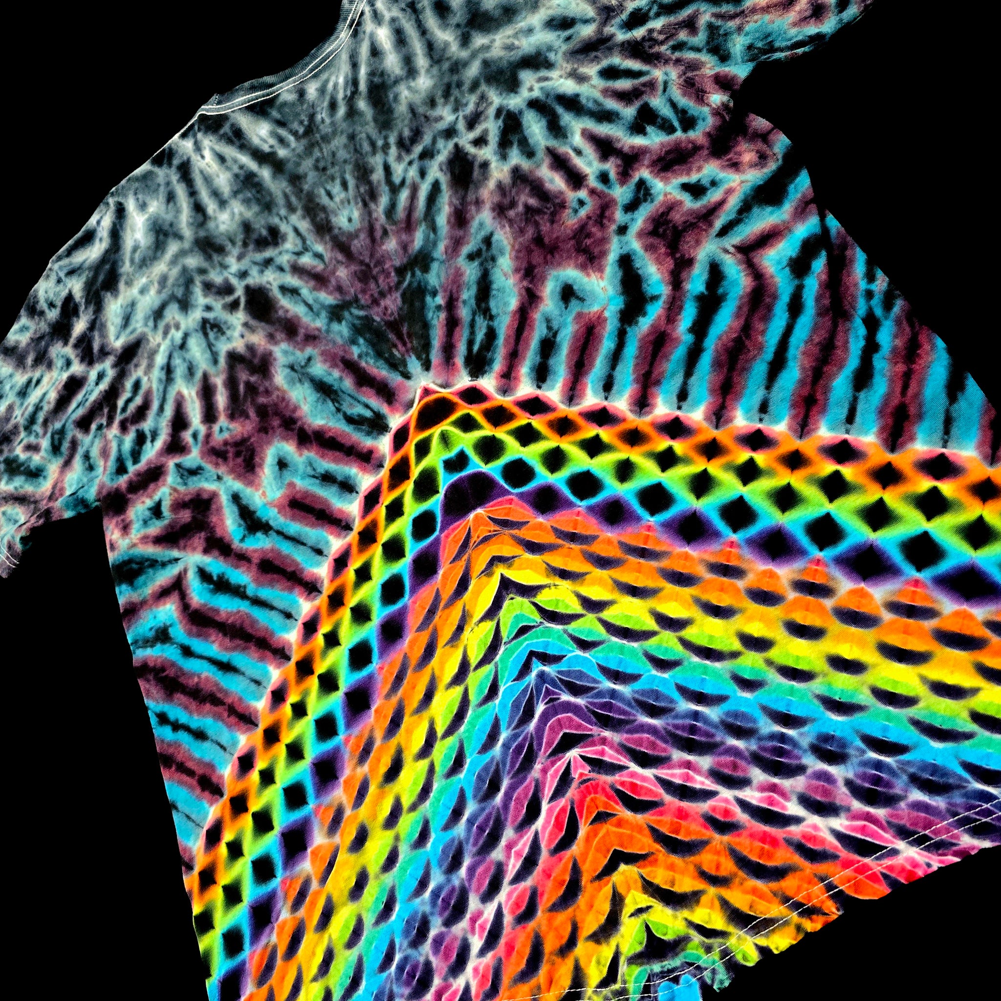 A close-up of a tie-dye t-shirt featuring a complex pattern of black, white, purple, and blue on the upper portion, transitioning into a vibrant rainbow geometric wave design on the lower portion, set against a solid black background.