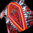 A close-up of a tie-dye t-shirt featuring a prominent central paisley-like motif with concentric hexagonal dots in red, orange, yellow, and purple, surrounded by black, white, and red marbled patterns.