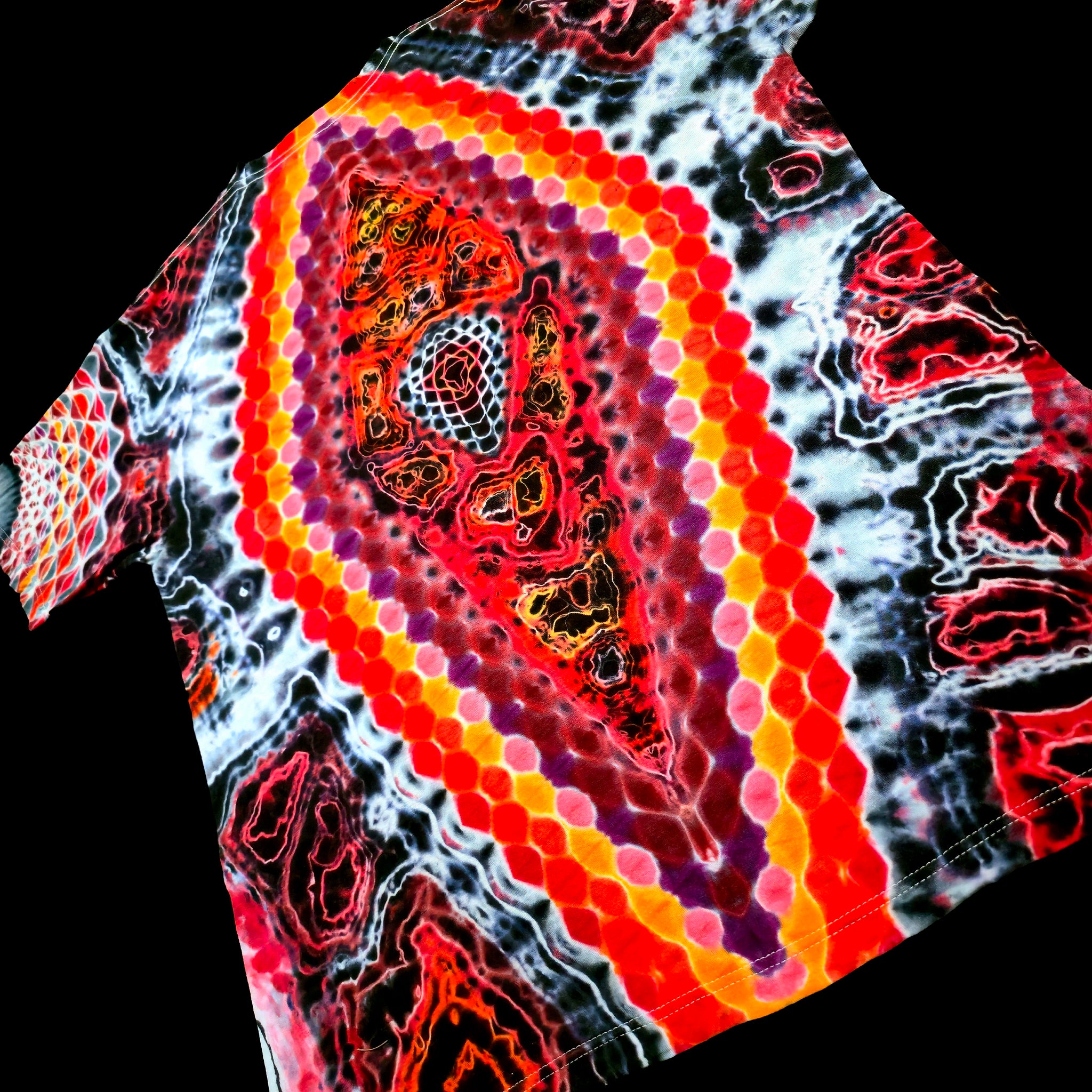 A close-up of a tie-dye t-shirt featuring a prominent central paisley-like motif with concentric hexagonal dots in red, orange, yellow, and purple, surrounded by black, white, and red marbled patterns.