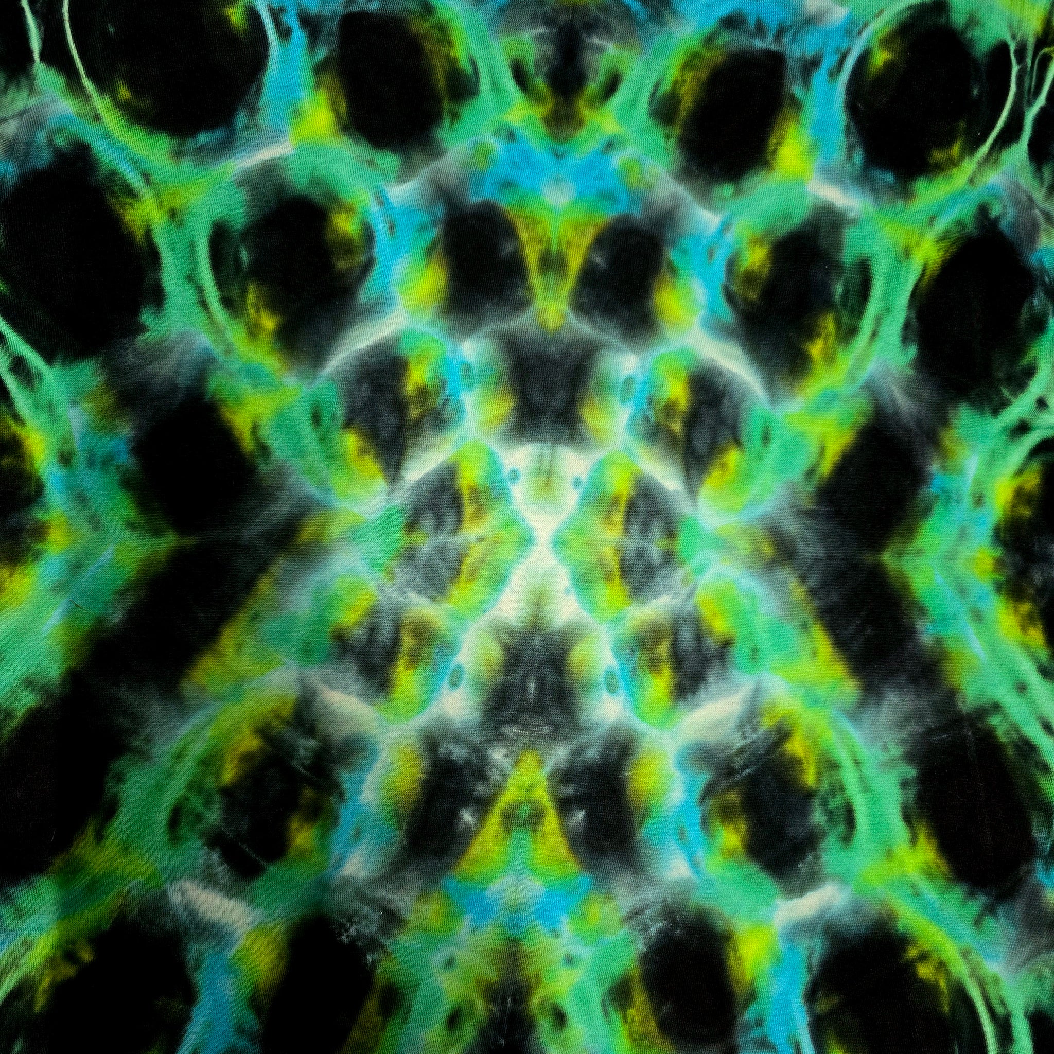 A close-up of a tie-dye fabric or material featuring a symmetrical, scale-like pattern in black, bright green, cyan, and yellow.