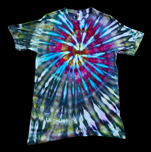 A short-sleeve crewneck tie-dye t-shirt featuring a vibrant spiral burst pattern in blue, magenta, yellow and pink against muted green and purple.  