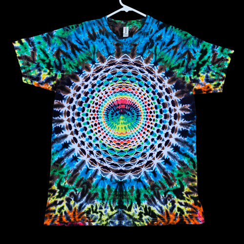 A short-sleeve t-shirt hanging on a white hanger against a solid black background, featuring a vibrant, symmetrical psychedelic mandala print with concentric circles and tie-dye patterns in blue, green, yellow, orange, pink, and white.