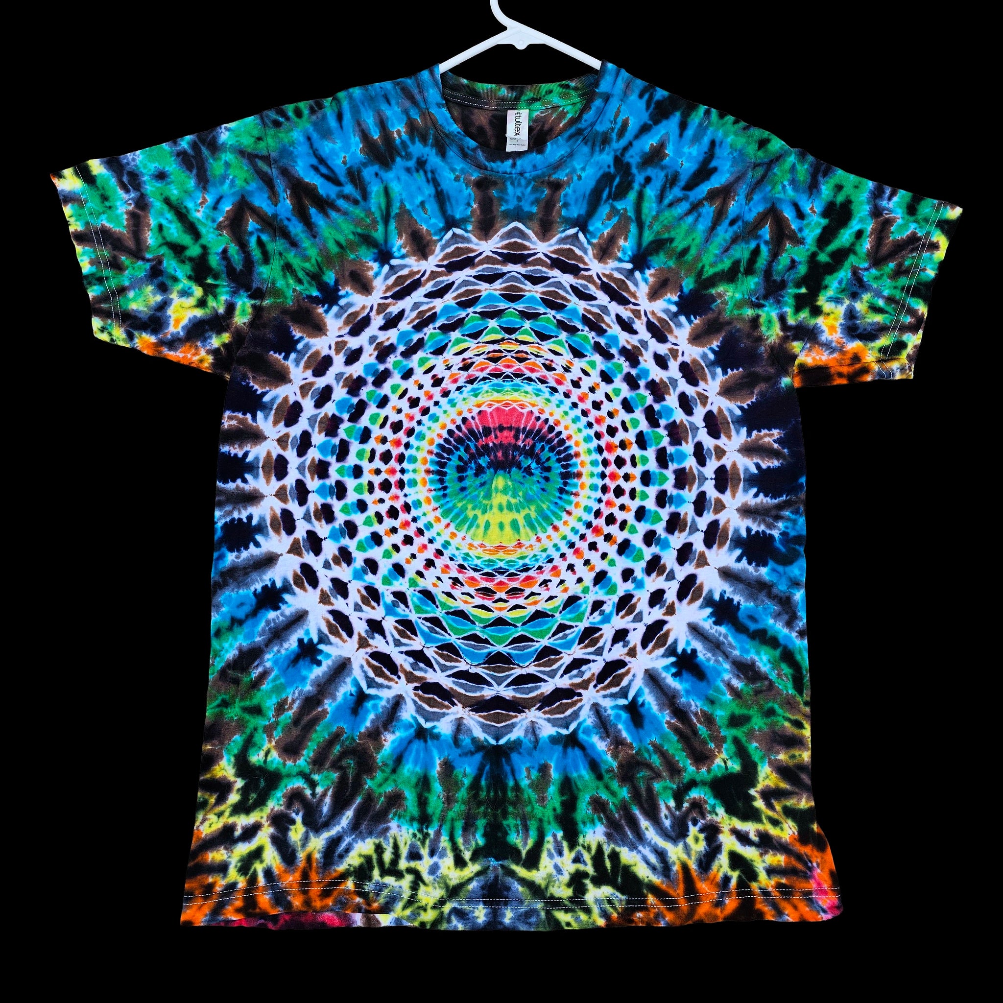 A short-sleeve t-shirt hanging on a white hanger against a solid black background, featuring a vibrant, symmetrical psychedelic mandala print with concentric circles and tie-dye patterns in blue, green, yellow, orange, pink, and white.