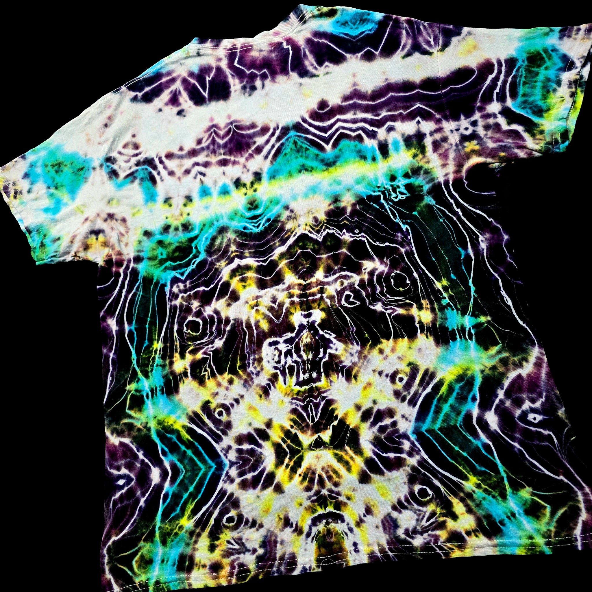 A short-sleeve crewneck t-shirt featuring a vibrant, symmetrical psychedelic tie-dye pattern with neon green, yellow, purple, and white on a black base, shown against a solid black background.
