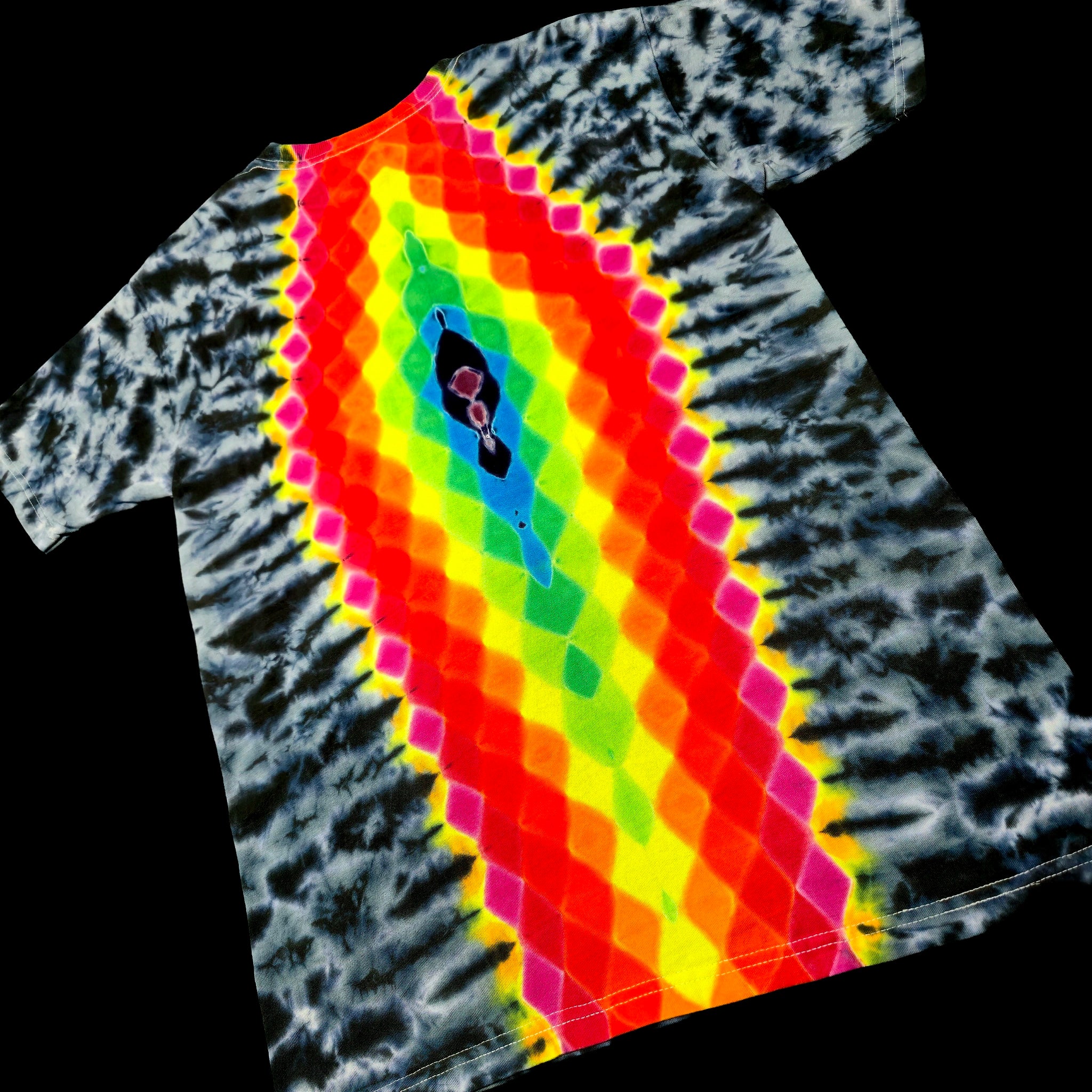 A tie-dye t-shirt with a vibrant rainbow gradient diamond pattern running diagonally from the collar to the hem, set against a solid black background.