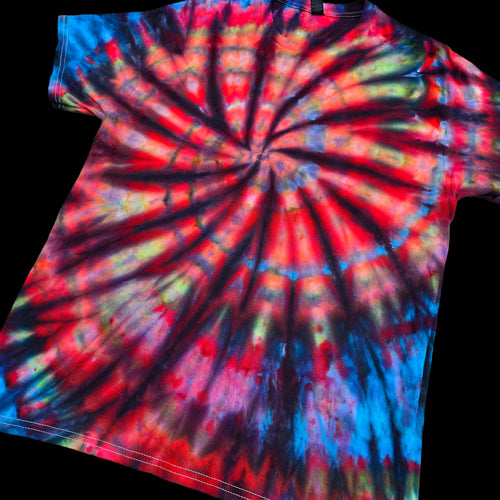 A short-sleeve tie-dye t-shirt featuring a vibrant spiral pattern with red, blue, yellow, and black dye blending together, shown against a solid black background.