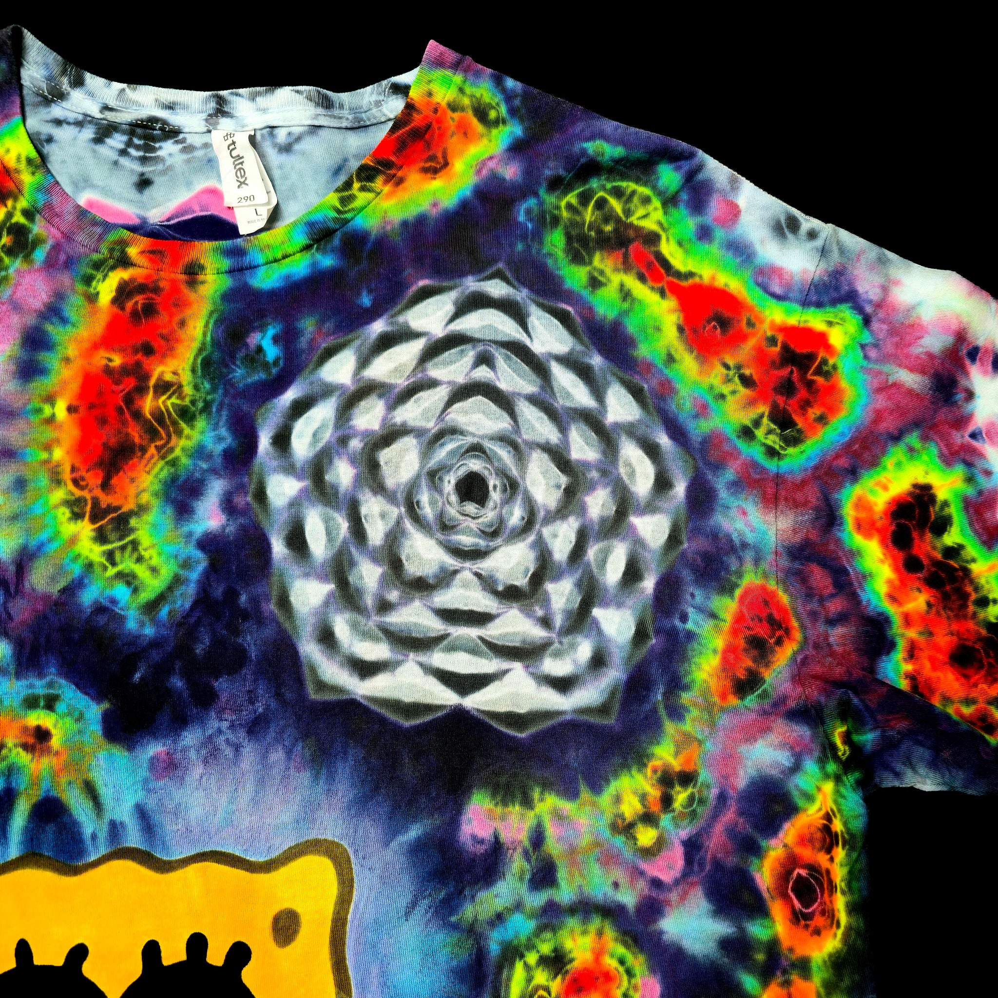 A close-up of a tie-dye t-shirt featuring a large white geometric flower design in the center, surrounded by vibrant neon rainbow tie-dye patterns, with a yellow graphic at the bottom.