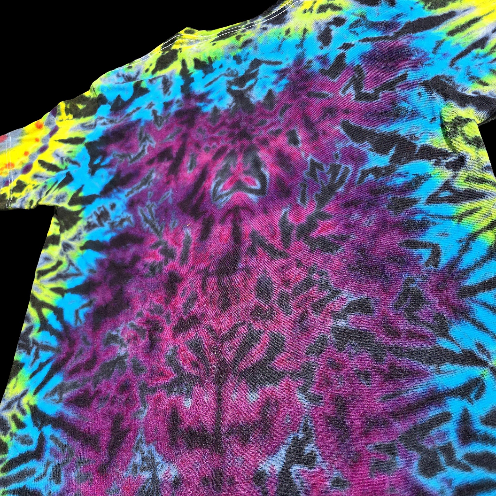 A close-up of a tie-dye t-shirt featuring a vibrant neon pattern of magenta pink, cyan blue, yellow, and black.