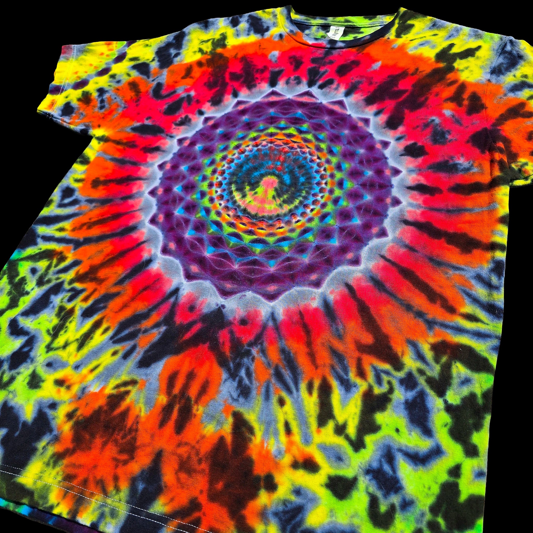 A short-sleeve crewneck t-shirt featuring a vibrant psychedelic spiral tie-dye pattern with neon yellow, green, orange, red, purple, and black, shown against a solid black background.