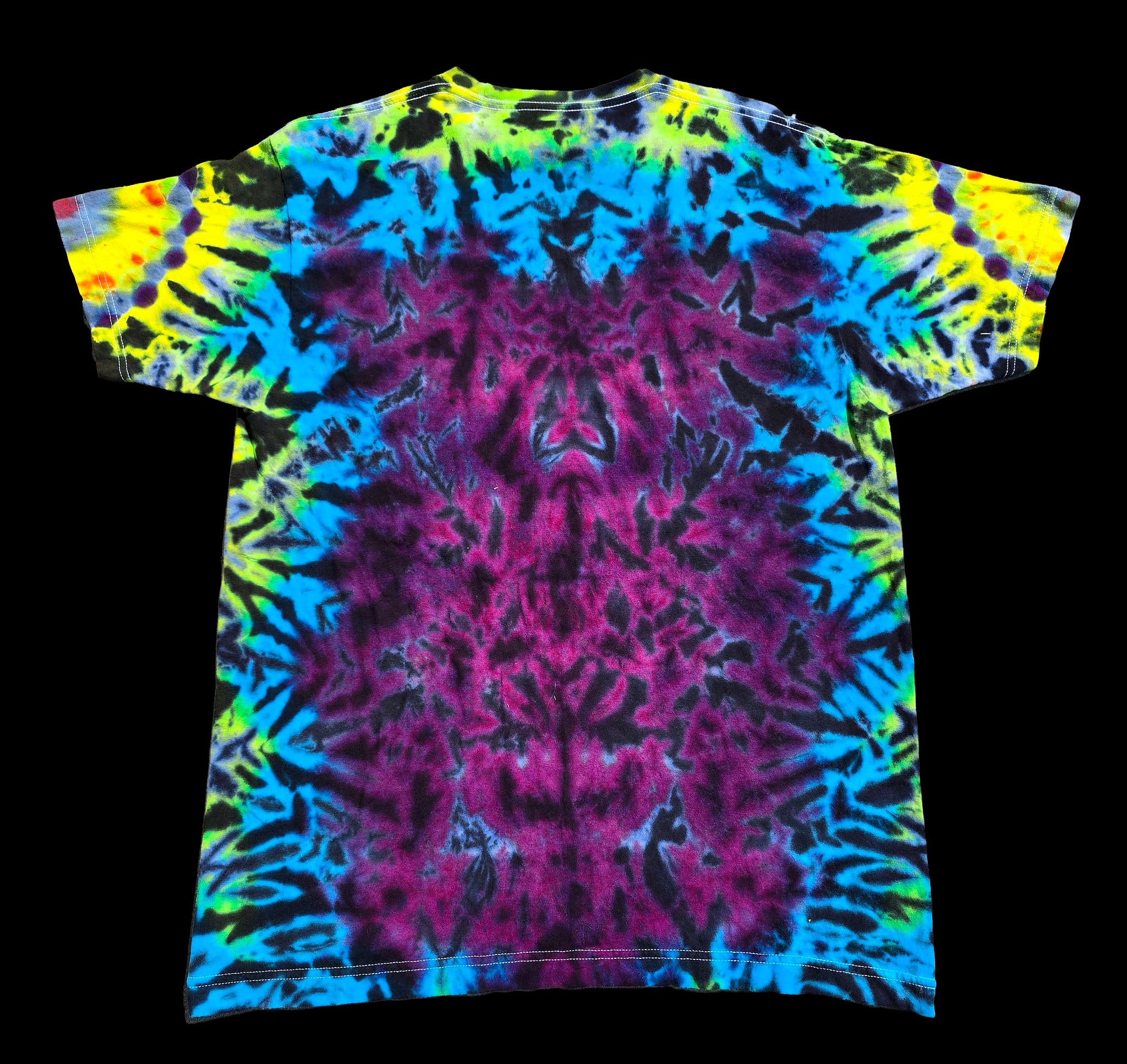 A short-sleeve tie-dye t-shirt displayed flat against a solid black background. The shirt features a vibrant, symmetrical tie-dye pattern with a large central magenta-purple area surrounded by concentric rings of bright blue, lime green, and yellow.