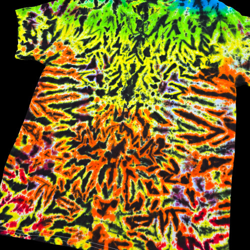 A short-sleeve tie-dye t-shirt with a highly vibrant, symmetrical mandala-like pattern in neon green, yellow, orange, red, and black, shown against a solid black background.