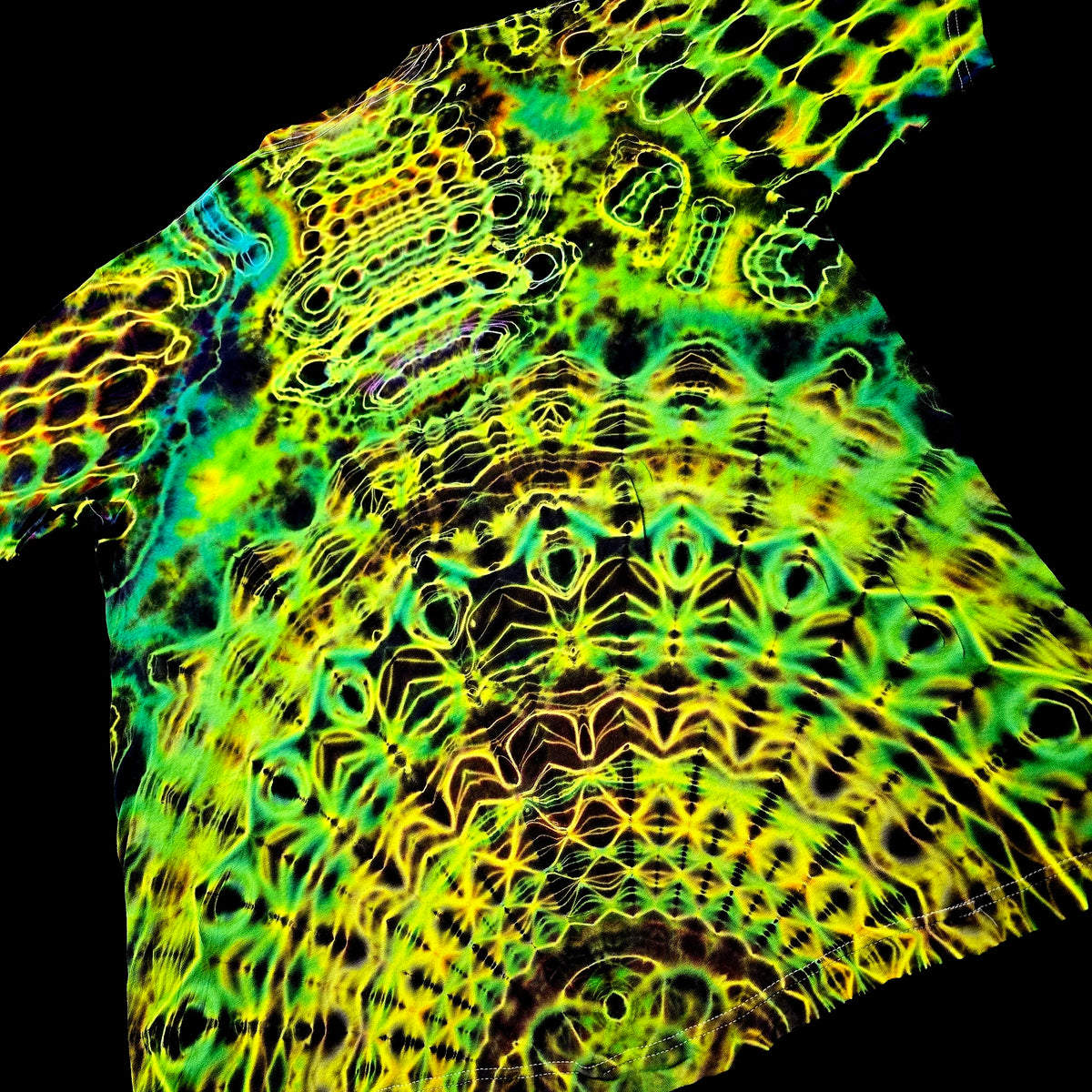 A close-up of a highly patterned fabric or material sample with a neon, fluorescent look. The design features intricate, symmetrical organic motifs in bright yellow, lime green, and cyan blue over a black background.