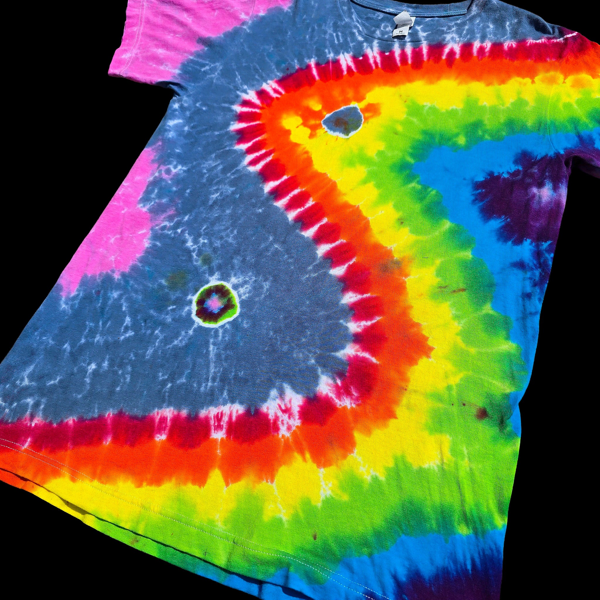 A short-sleeve tie-dye T-shirt. The shirt features a large, stylized wave pattern in a rainbow of colors including pink, blue, yellow, green, orange, and purple, with two small circular holes. with matching back.