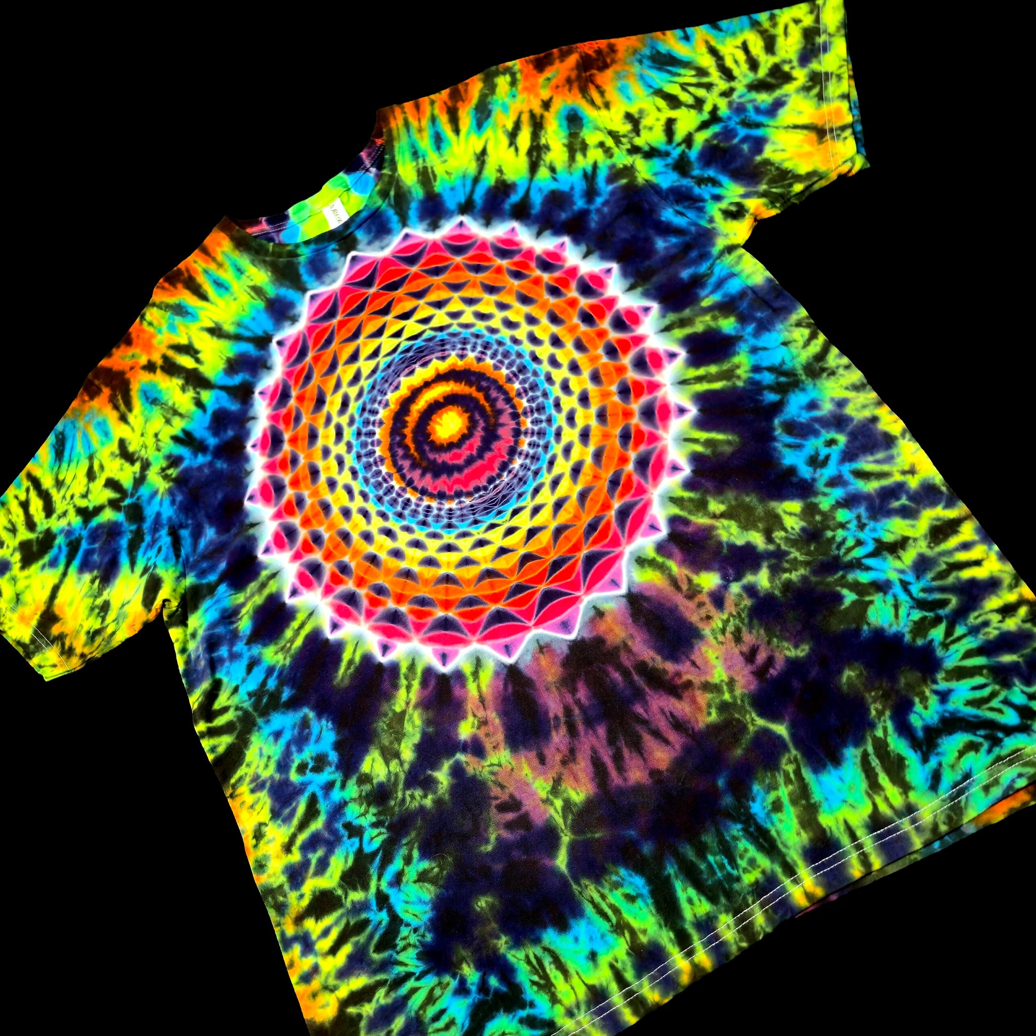 A short-sleeve tie-dye T-shirt laid flat on a black background, featuring a large psychedelic mandala spiral pattern in neon yellow, green, blue, purple, pink, and orange.