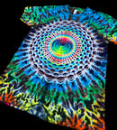 A short-sleeve tie-dye T-shirt laid flat on a black background, featuring a large circular mandala-style rainbow print with blue, green, yellow, red, orange, and white patterns.