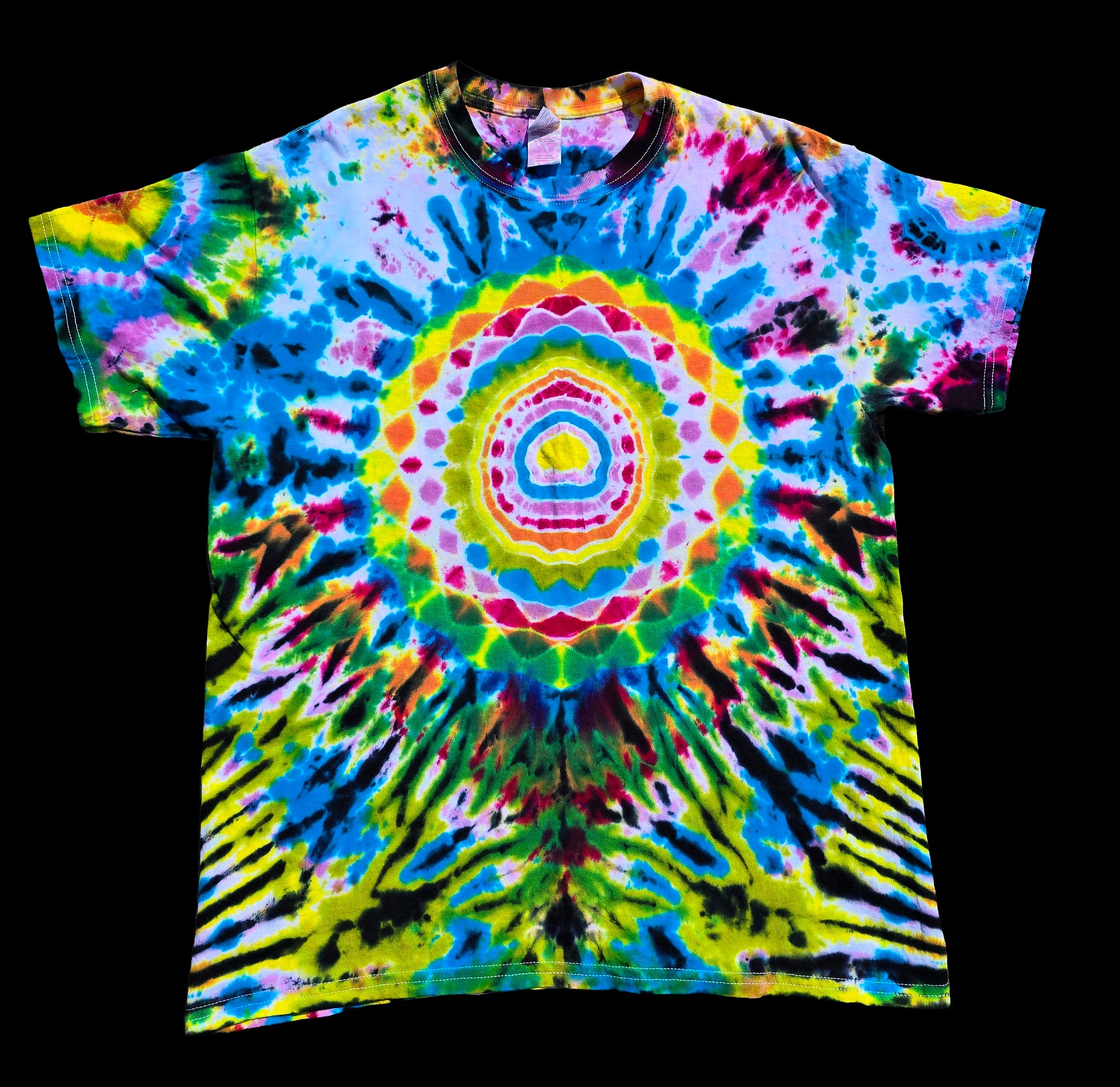 A short-sleeve crewneck tie-dye t-shirt featuring a vibrant psychedelic mandala pattern with concentric circles and radiating stripes in neon yellow, green, blue, pink, purple, and black, displayed flat against a solid black background.