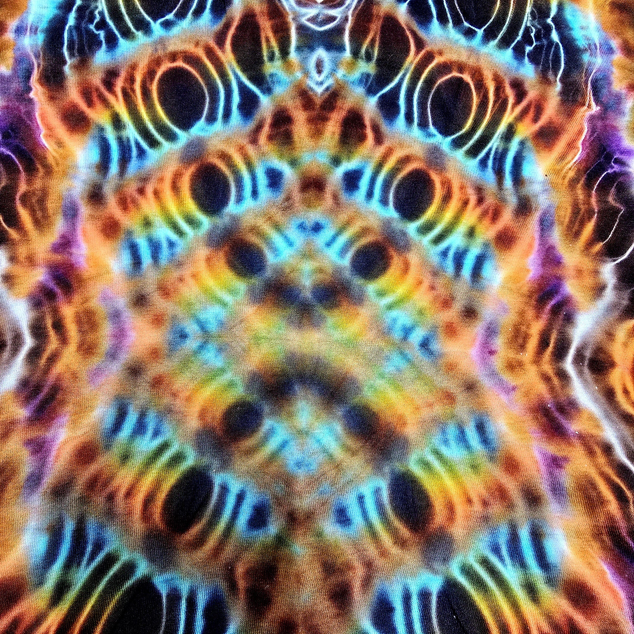 A close-up of a highly saturated abstract pattern with symmetrical concentric rings and wavy lines in bright cyan, orange, yellow, purple, and black, filling the entire frame.