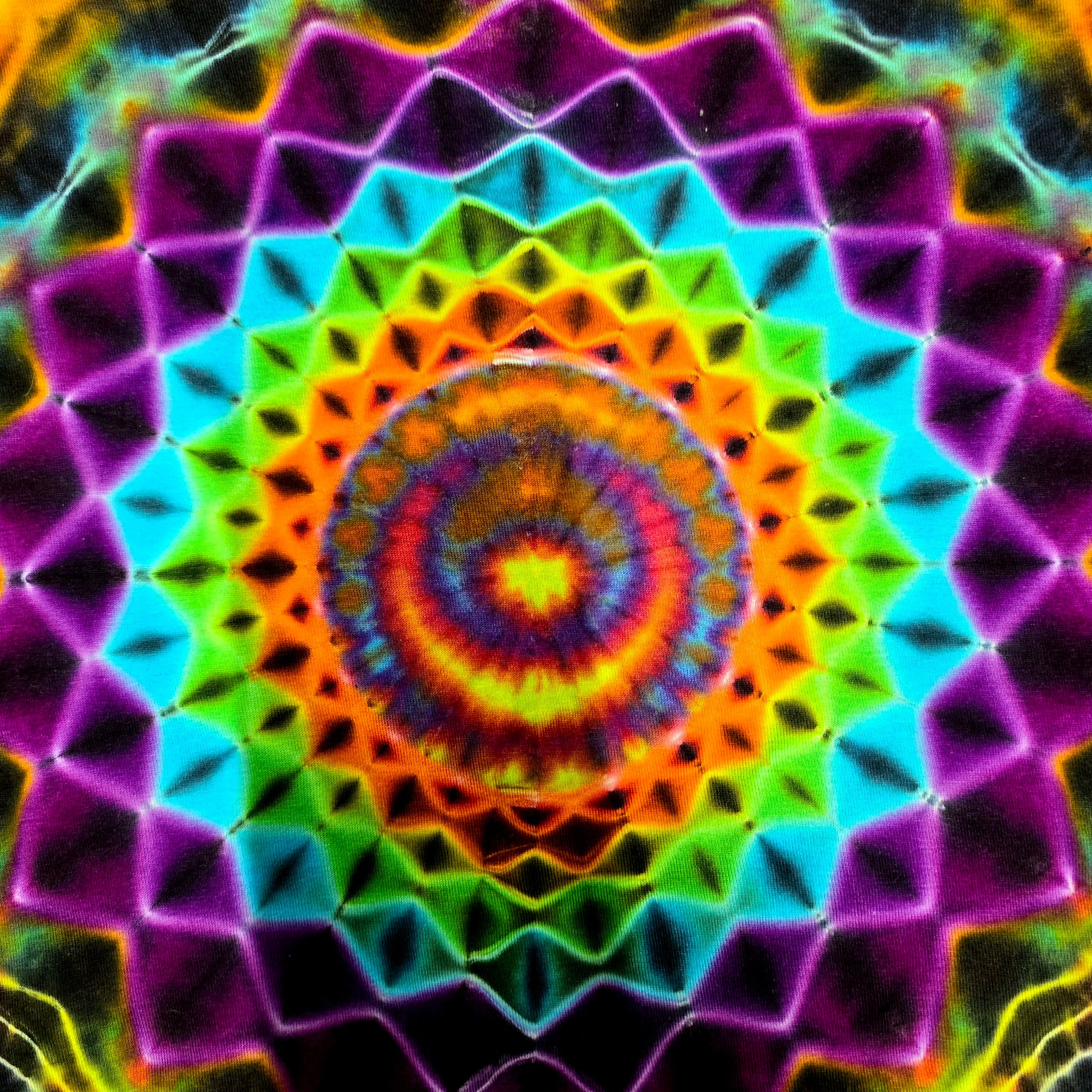 A vibrant, symmetrical psychedelic mandala pattern with concentric rings of neon purple, cyan, green, orange, yellow, and red on a dark background.