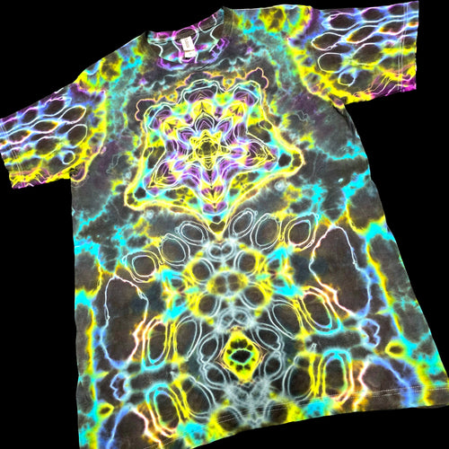 A short-sleeve crewneck t-shirt featuring a vibrant, symmetrical psychedelic kaleidoscope pattern with neon yellow, cyan, purple, and white glowing lines over a dark base.