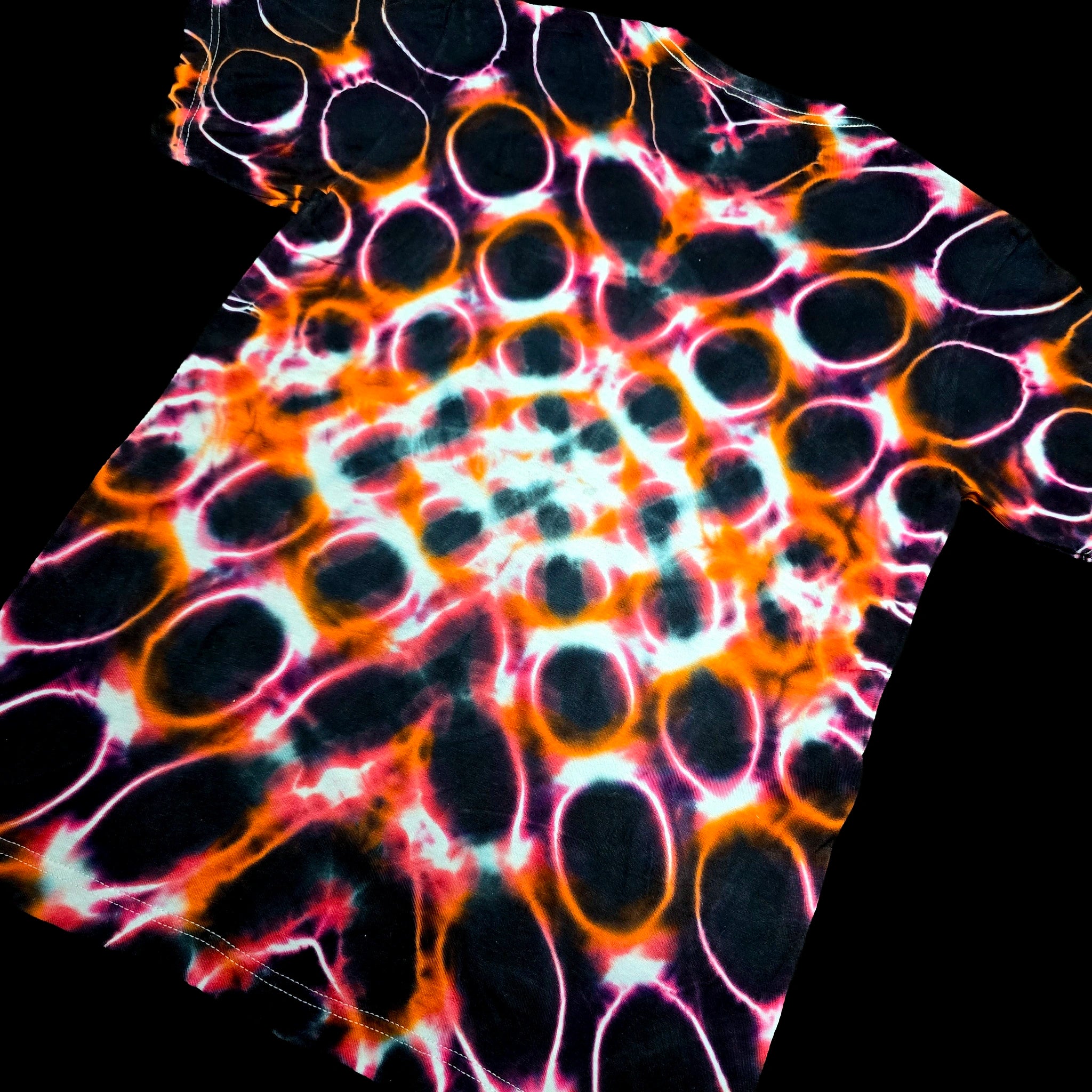 A short-sleeve t-shirt featuring a vibrant, high-contrast tie-dye pattern of black circles outlined in bright neon orange, pink, and white, set against a solid black background.