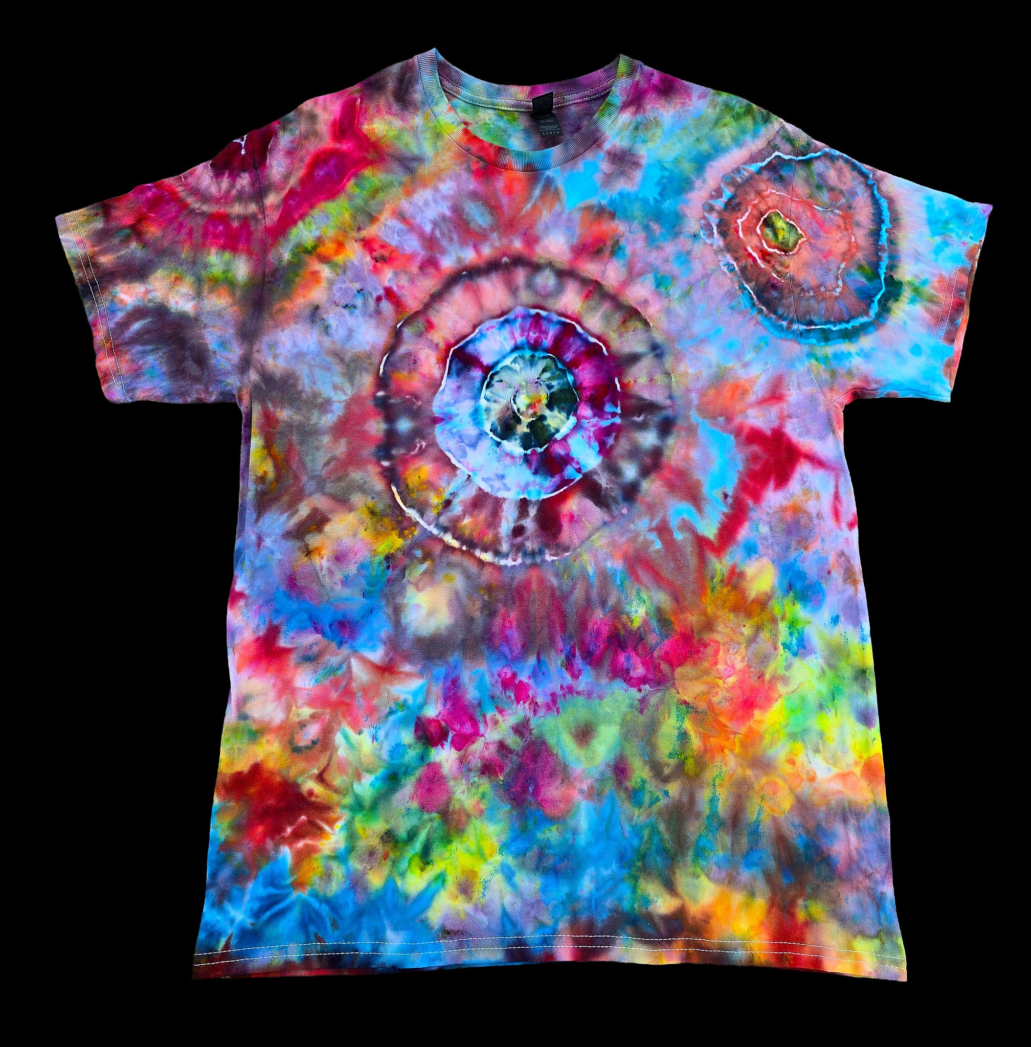 A short-sleeve crewneck tie-dye t-shirt featuring a large spiral pattern in the center and a smaller circular motif on the upper right chest, displayed flat against a solid black background.