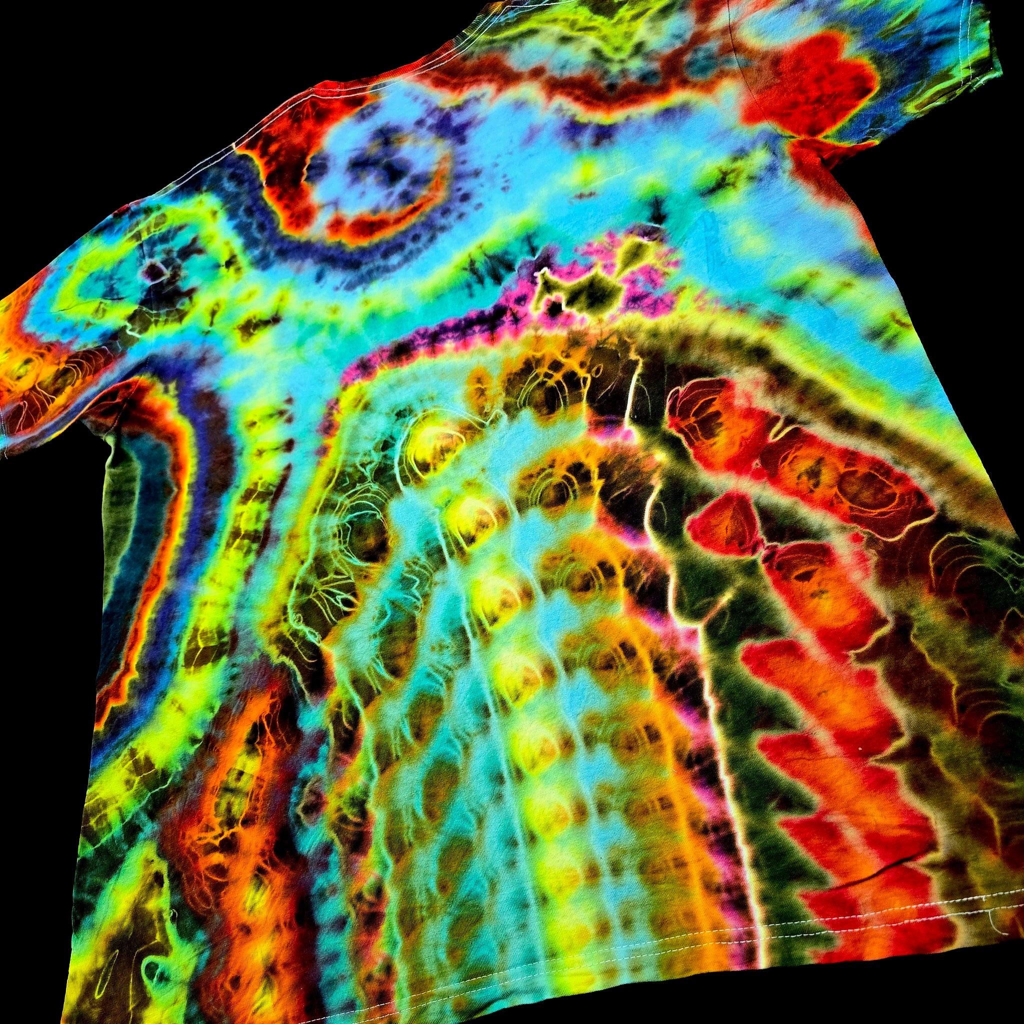 A short-sleeve tie-dye T-shirt laid flat on a black background, featuring a vivid multicolor agate-geode-inspired pattern with swirling bands of blue, green, yellow, orange, red, and purple.