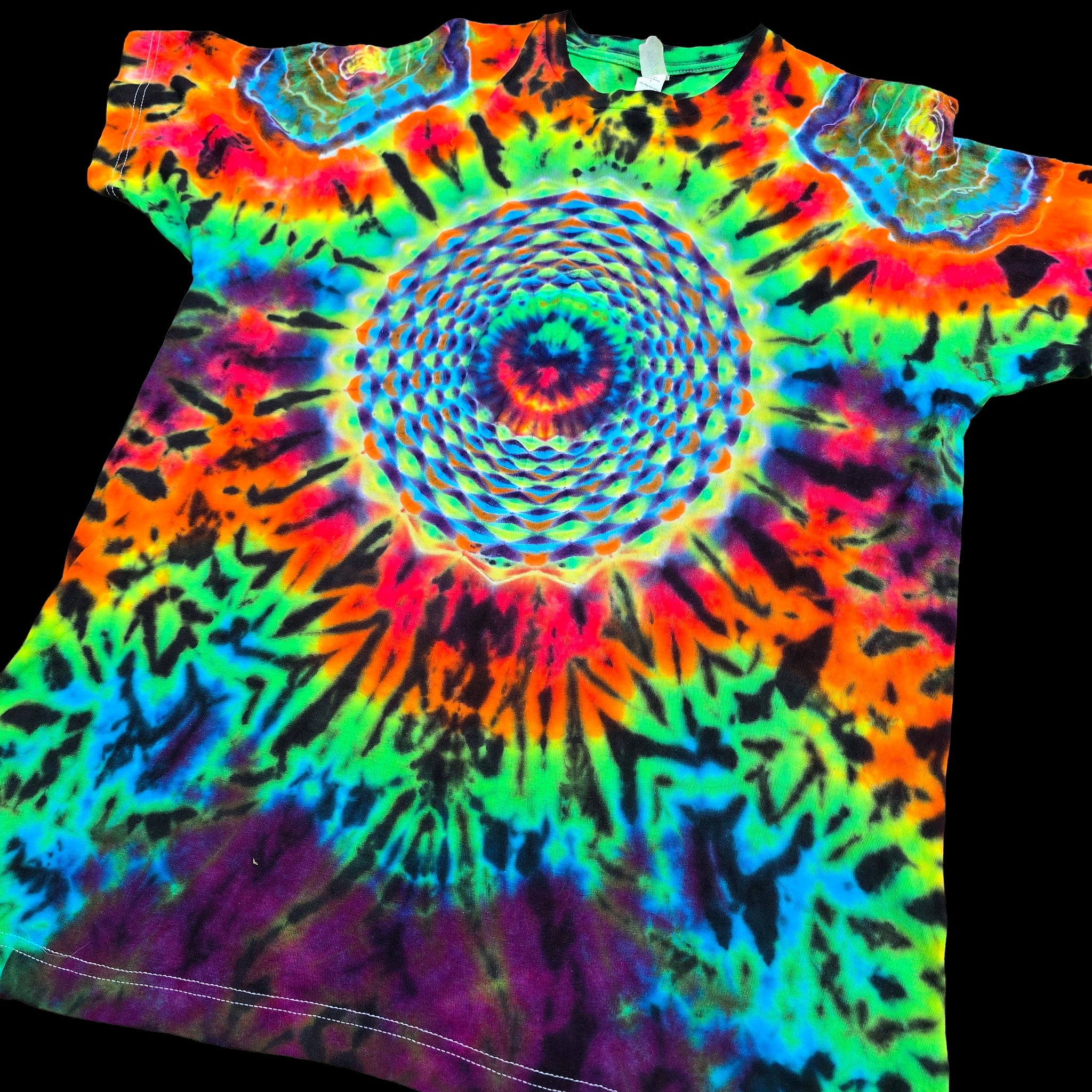 A short-sleeve tie-dye T-shirt laid flat on a black background, featuring a large spiral rainbow pattern with neon blue, green, yellow, orange, pink, purple, and black.