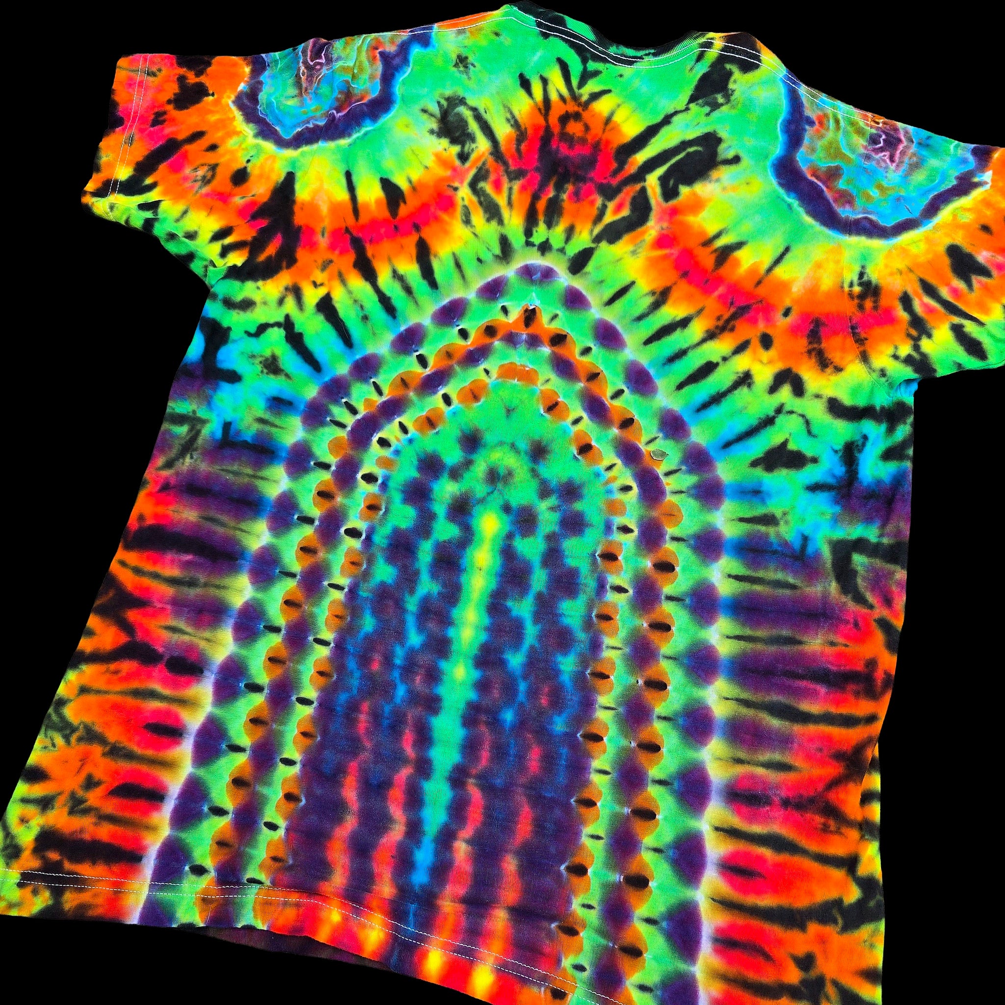 A short-sleeve tie-dye t-shirt with a psychedelic, high-contrast pattern featuring concentric arches and circular motifs in neon green, blue, purple, orange, yellow, and red, shown against a solid black background.