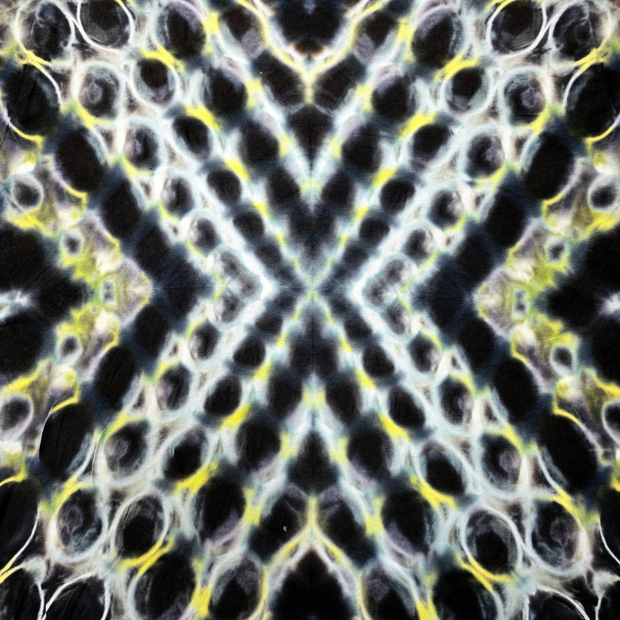 A close-up of a textured fabric or material pattern with a symmetrical, kaleidoscopic design featuring black, white, yellow, and gray tones.