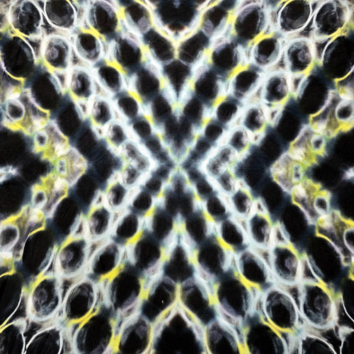 A close-up of a textured fabric or material pattern with a symmetrical, kaleidoscopic design featuring black, white, yellow, and gray tones.