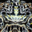 A close-up of a black short-sleeve t-shirt featuring a highly symmetrical, psychedelic tie-dye pattern with white, yellow, and orange organic swirls.