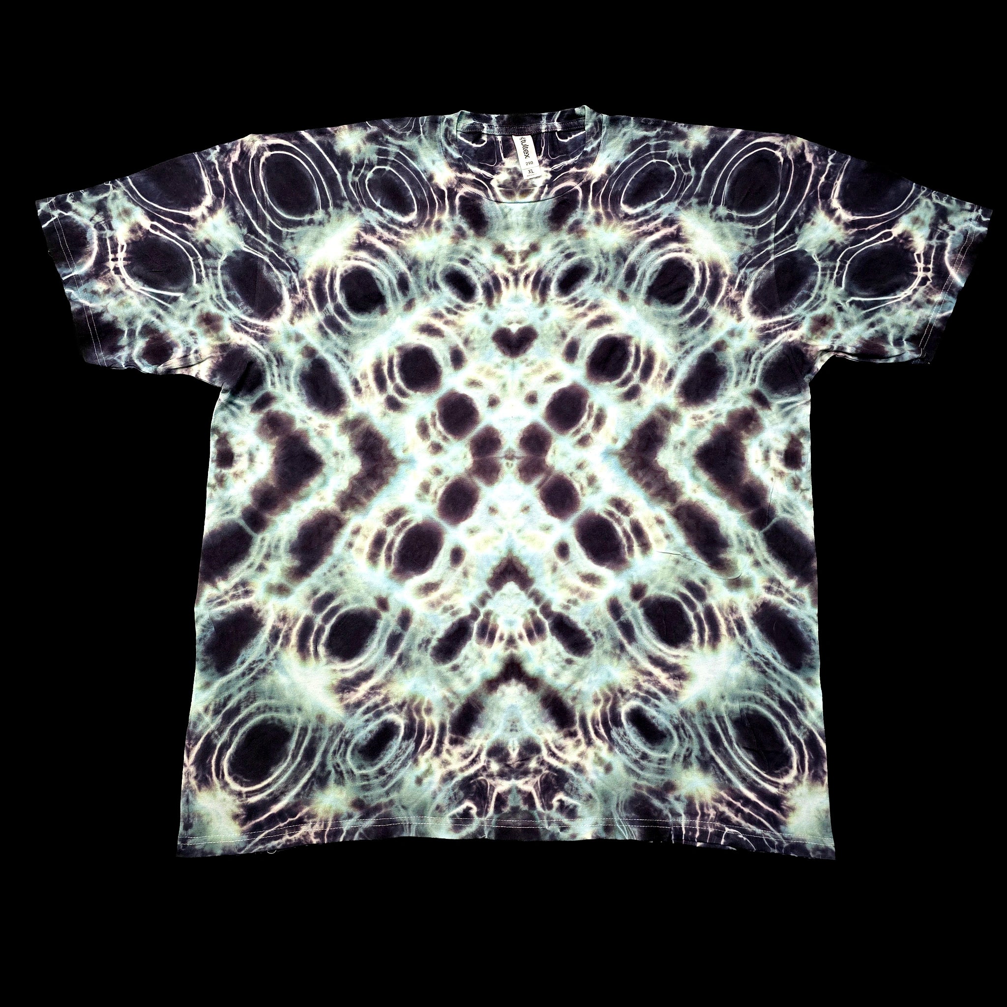 A short-sleeve crewneck t-shirt featuring a symmetrical, kaleidoscopic abstract pattern of black, white, and pale green circles, photographed flat against a solid black background.