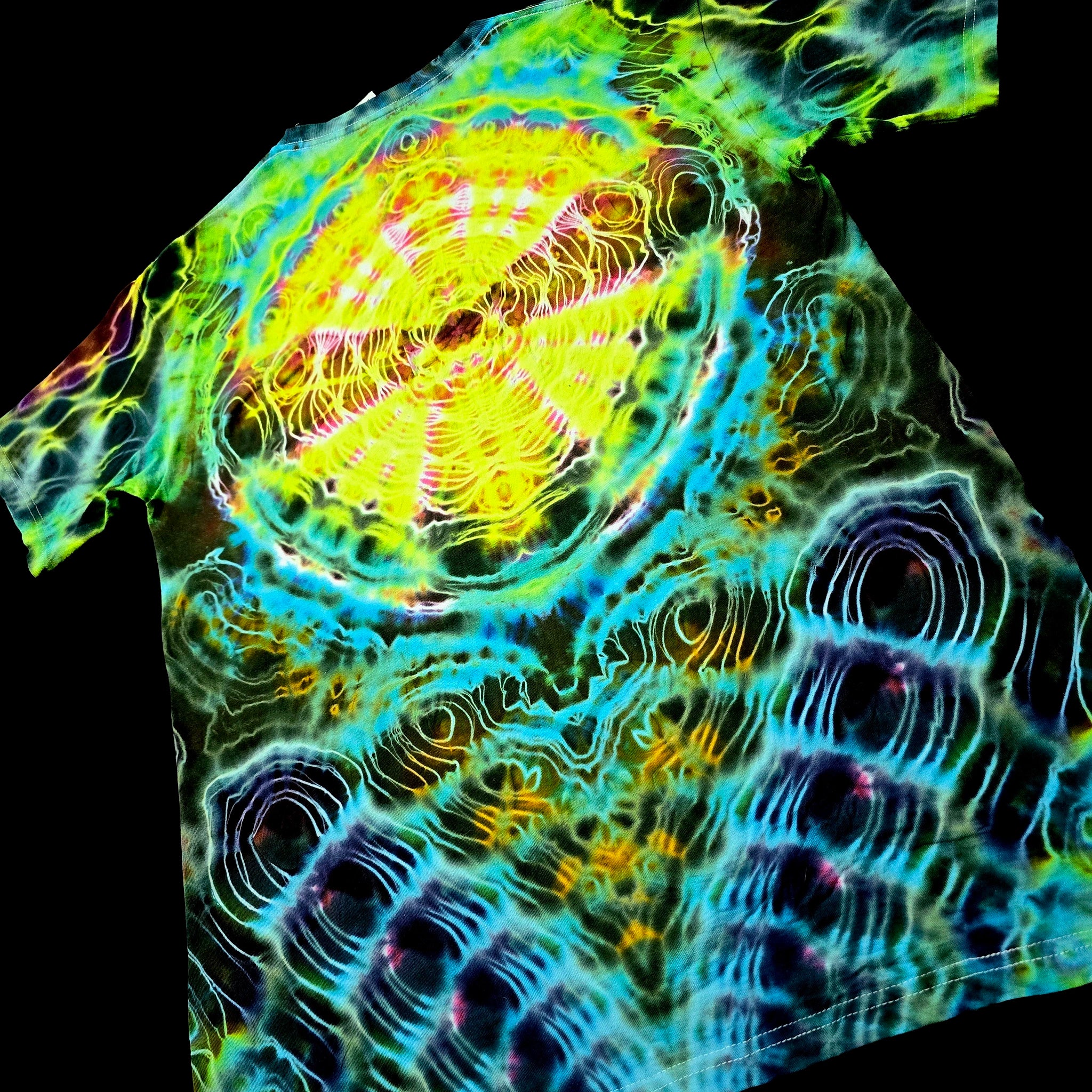 A short-sleeve t-shirt with an all-over psychedelic, high-contrast abstract pattern featuring bright yellow, cyan, green, and purple concentric wave-like designs on a black background.