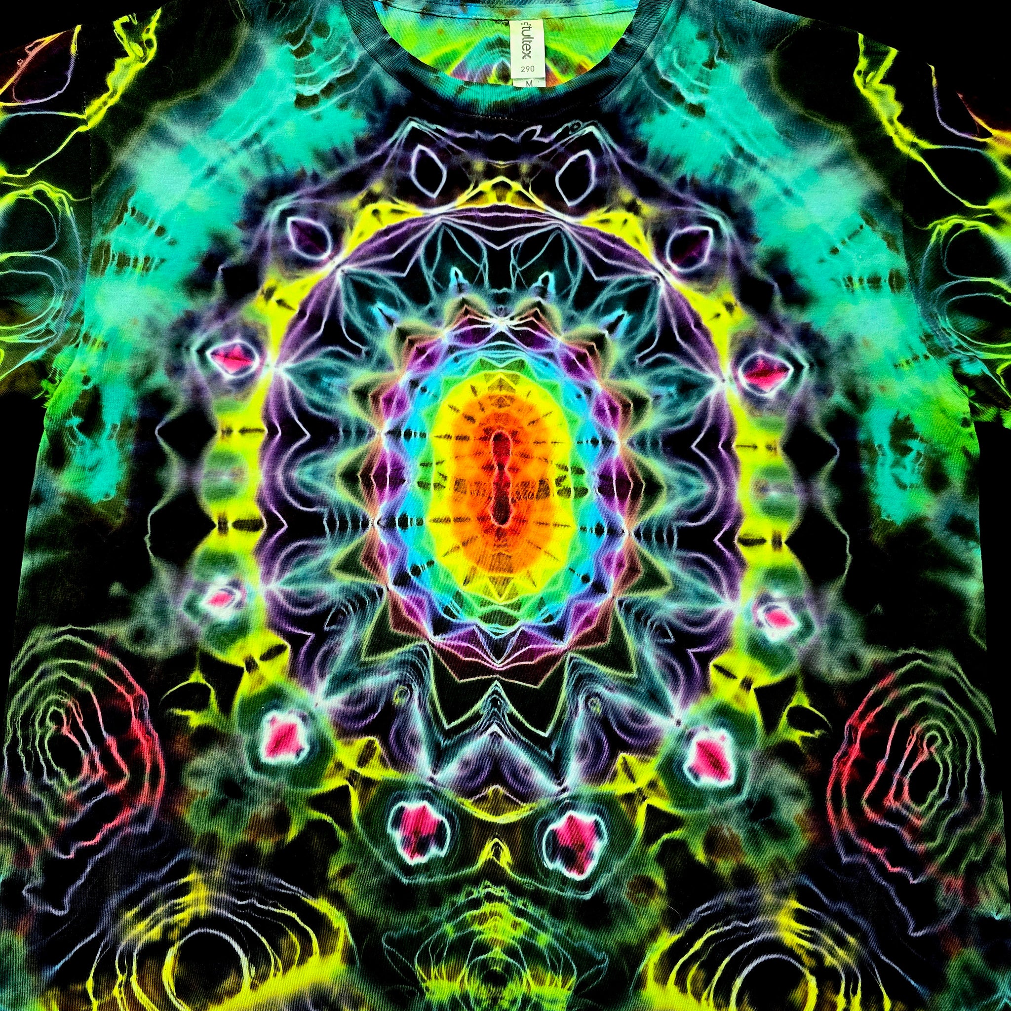 A close-up of a tie-dye t-shirt featuring a highly symmetrical, psychedelic mandala pattern with neon green, yellow, purple, blue, and pink colors on a black base.