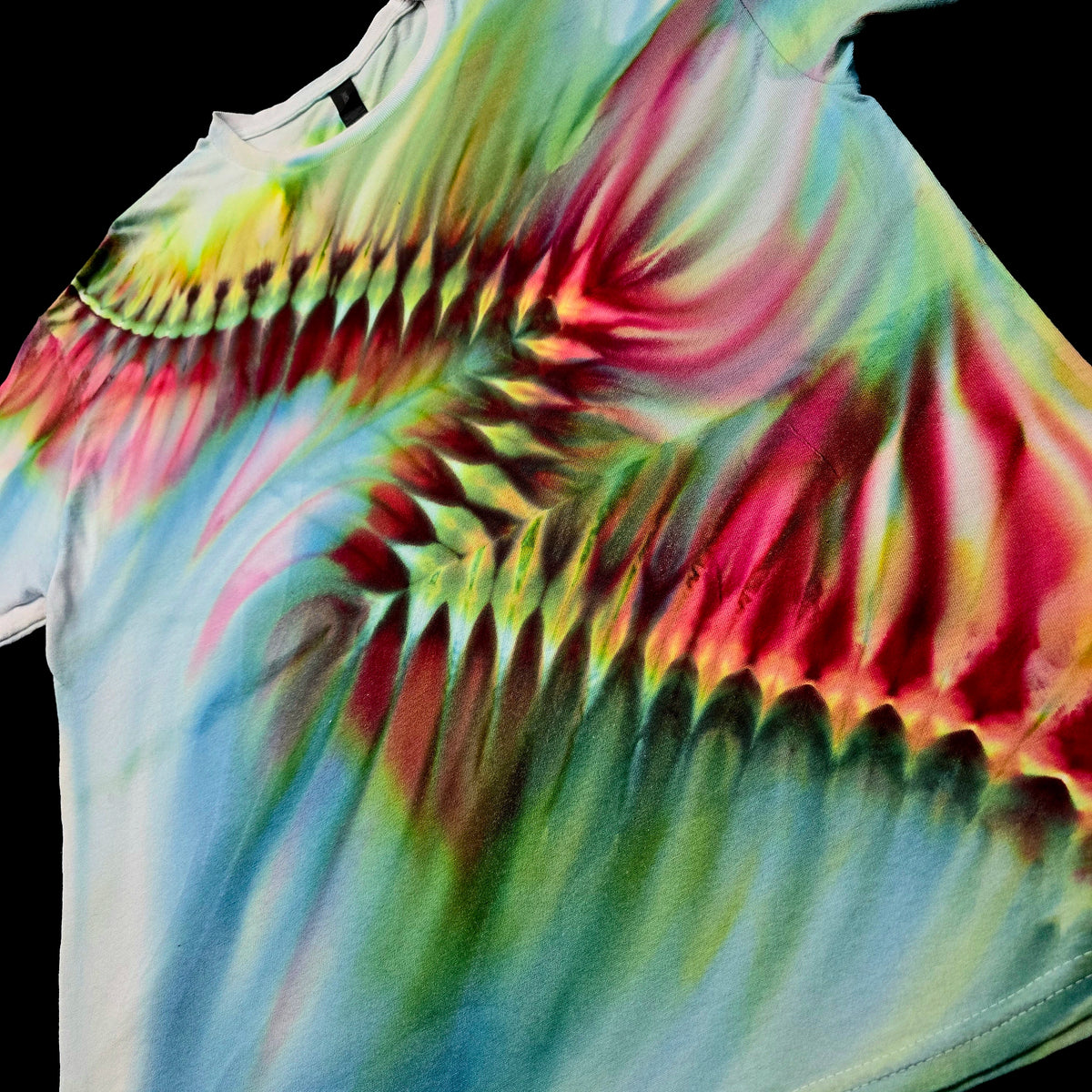 A close-up of a tie-dye t-shirt featuring a vibrant, swirling pattern of pink, green, yellow, and blue on a black background.